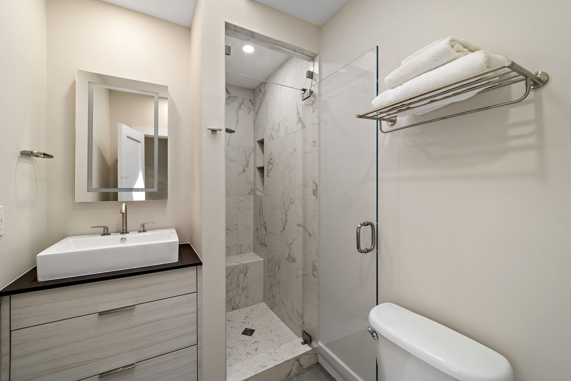 Hall bath with floating vanity, LED mirror, marble tile shower, glass door, and brushed nickel fixtures