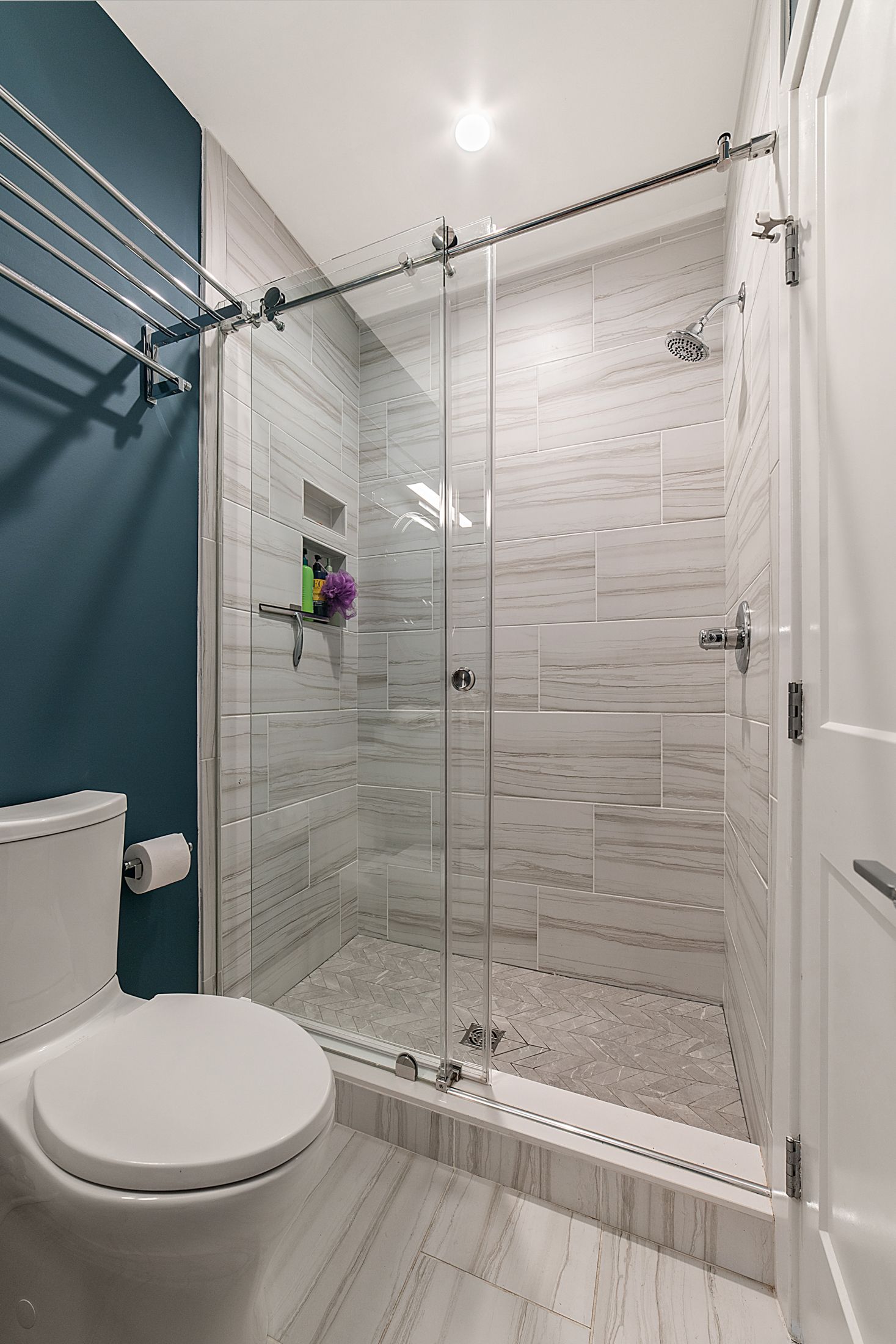 Modern bathroom with walk-in shower, glass door, teal accent wall, porcelain tile walls, and herringbone shower floor