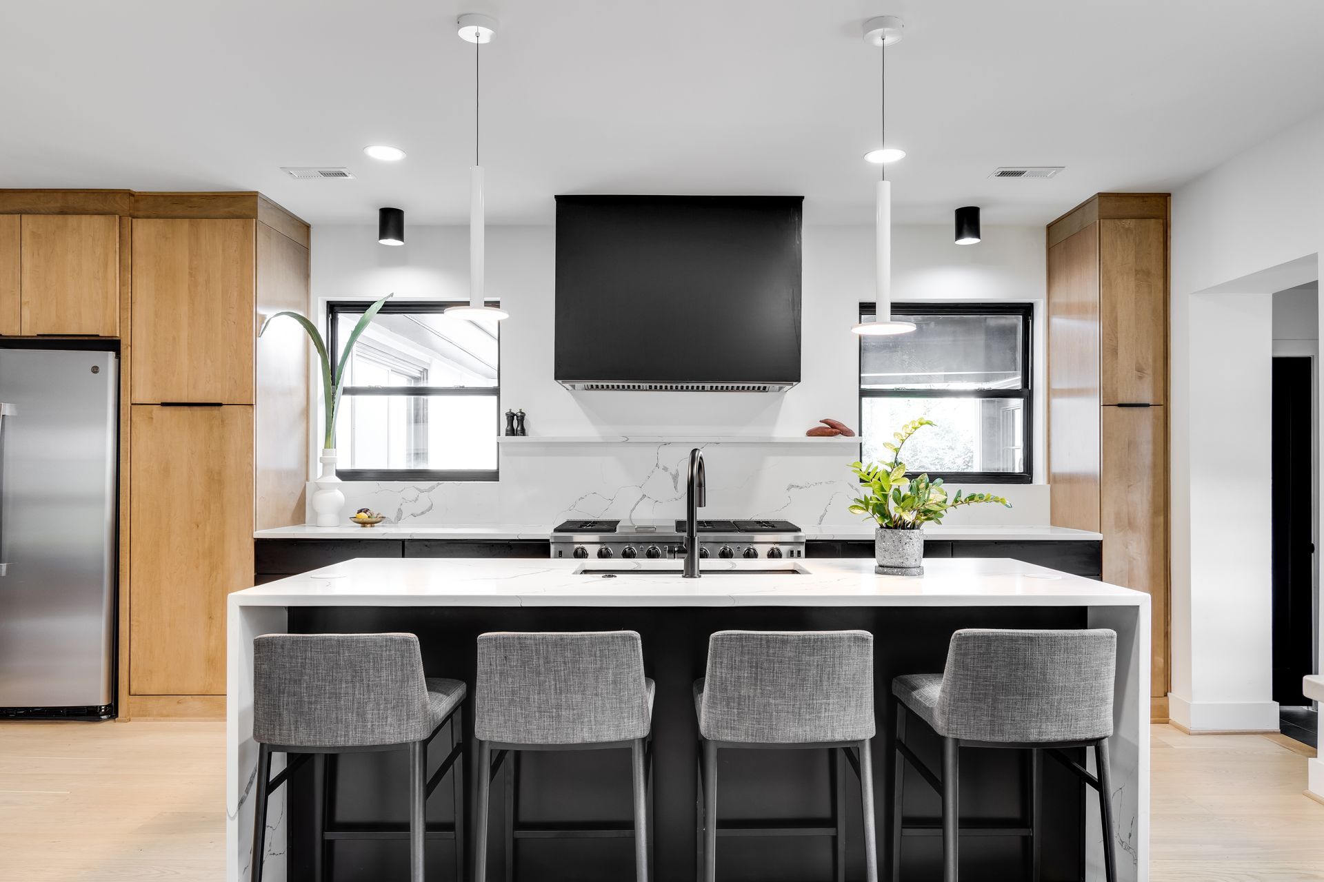Modern kitchen with black and white island, bar seating, wood cabinetry, and minimalist pendant lighting