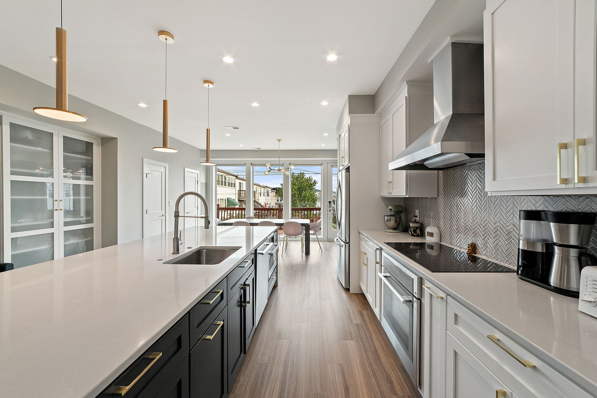 Modern kitchen with white cabinets, large island, herringbone backsplash, and brass pendant lights