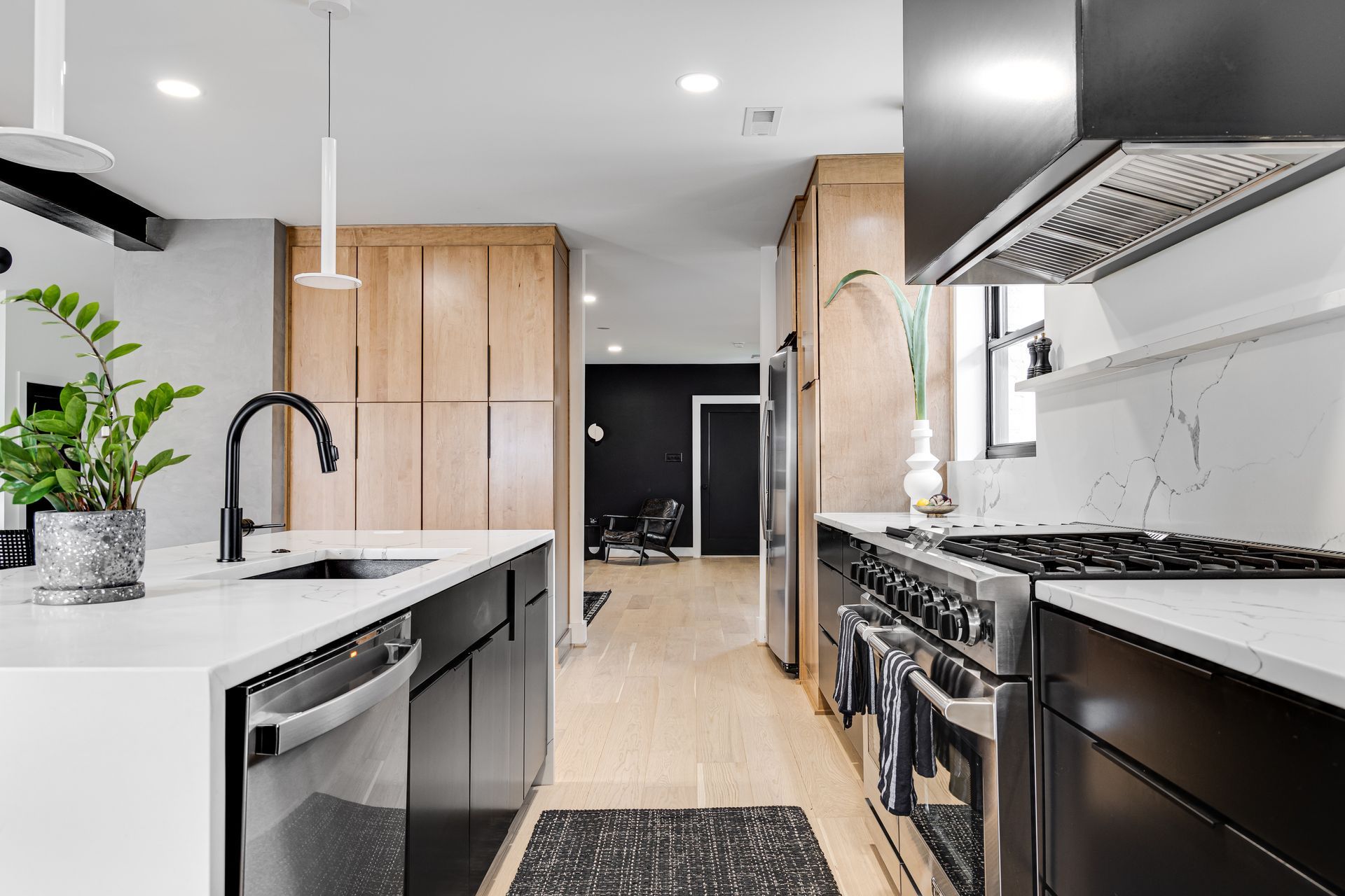Wide-angle view of modern kitchen with black and wood cabinets, waterfall island, and stainless appliances