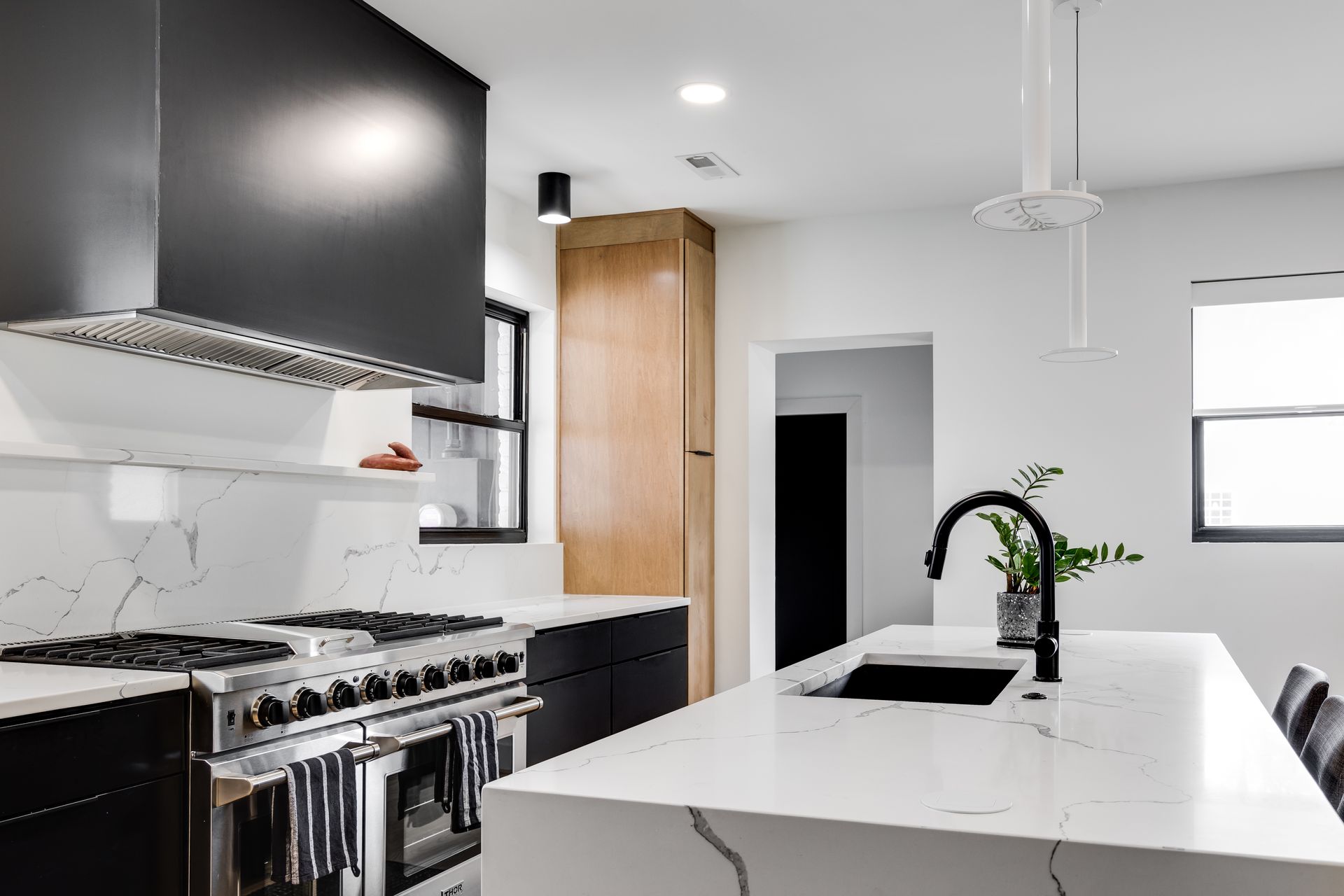 Modern kitchen with black hood, white marble waterfall island, matte black faucet, and stainless steel range