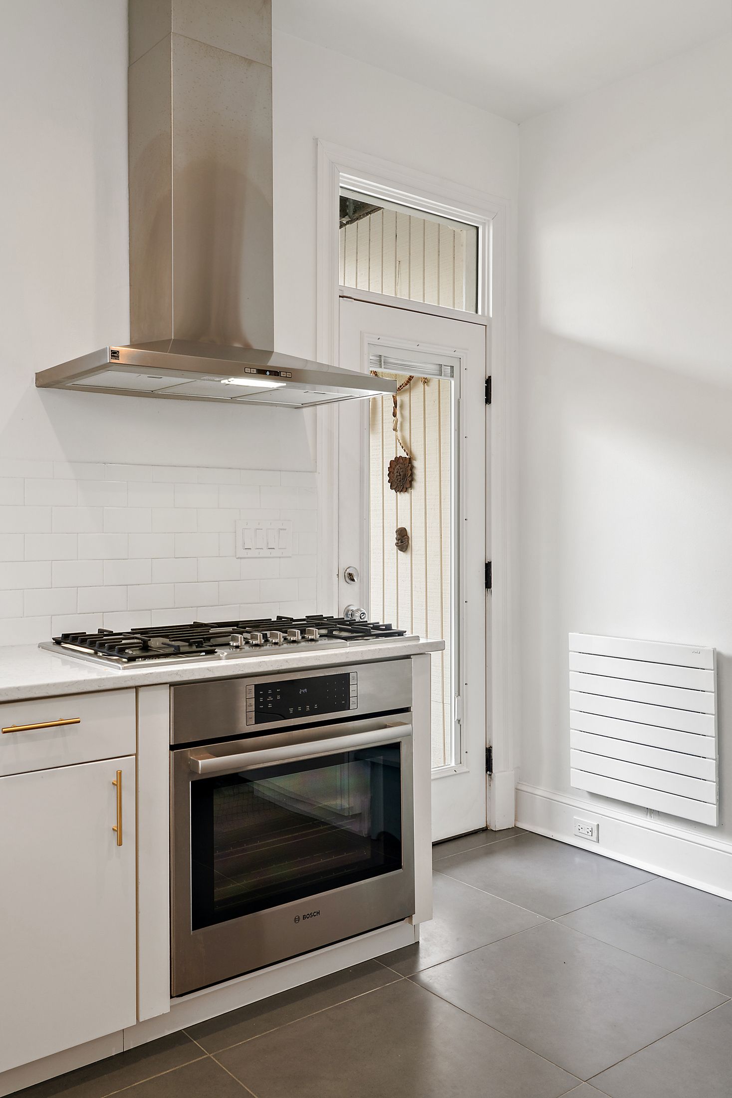 Stainless steel gas range with matching hood in a white kitchen, featuring a subway tile backsplash and a glass-paneled back door.