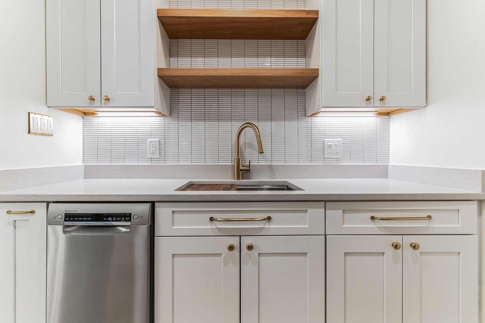white kitchen remodel with gold faucet, open wood shelves, modern backsplash, and under-cabinet lighting