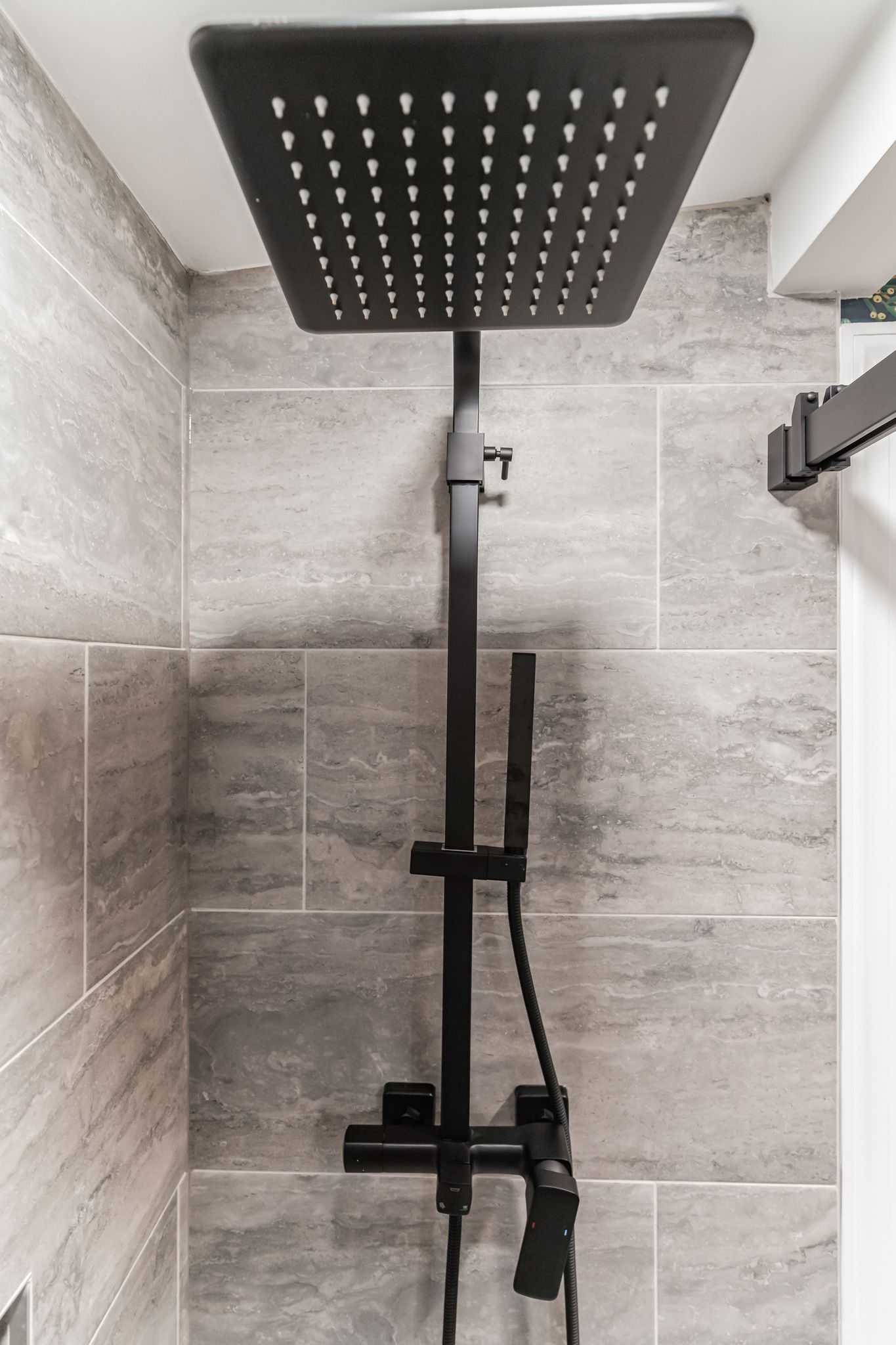 matte black rain shower head with handheld attachment on gray tile wall