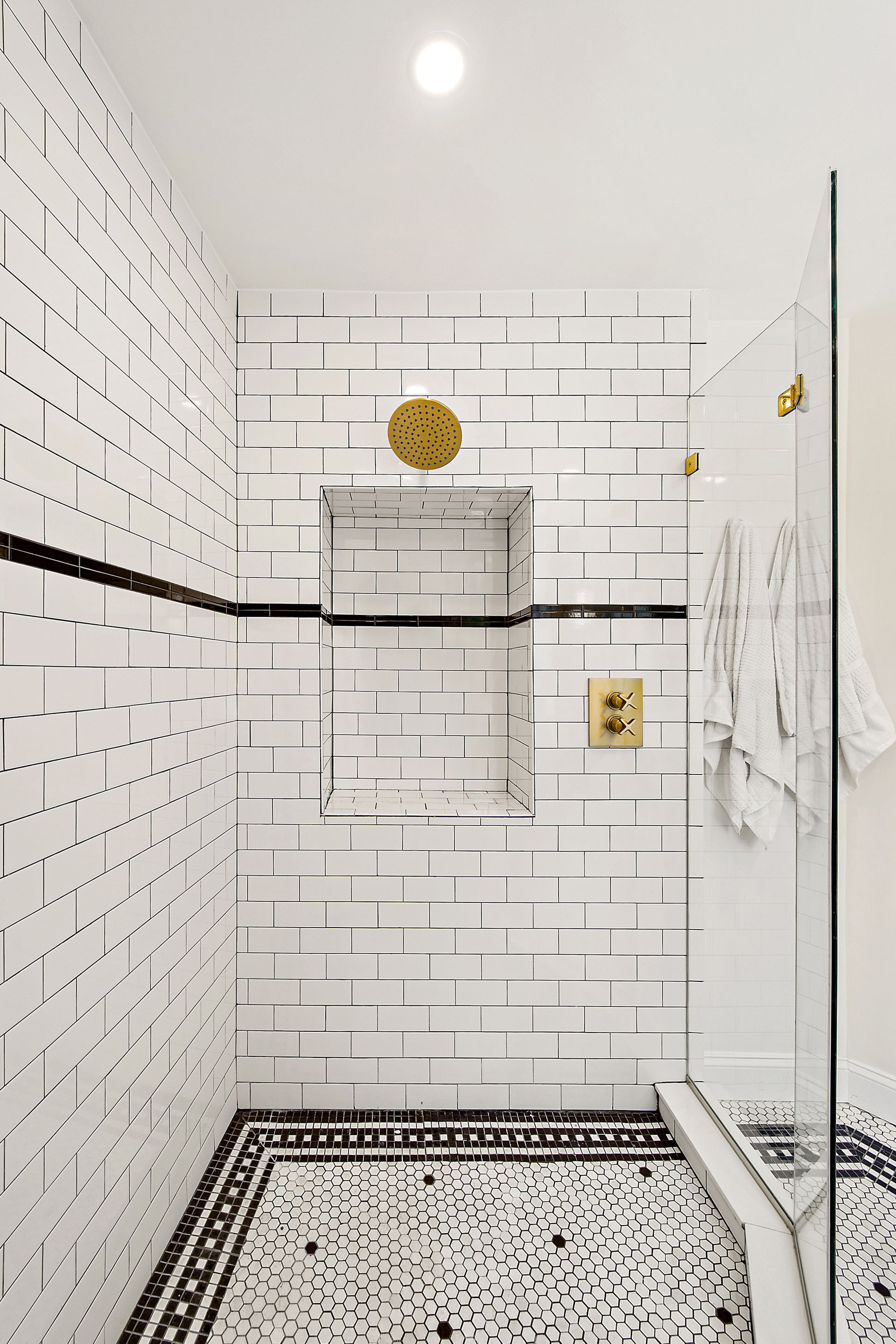 white subway tile shower with gold showerhead, shower niche, vintage mosaic tile floor, and black accent line