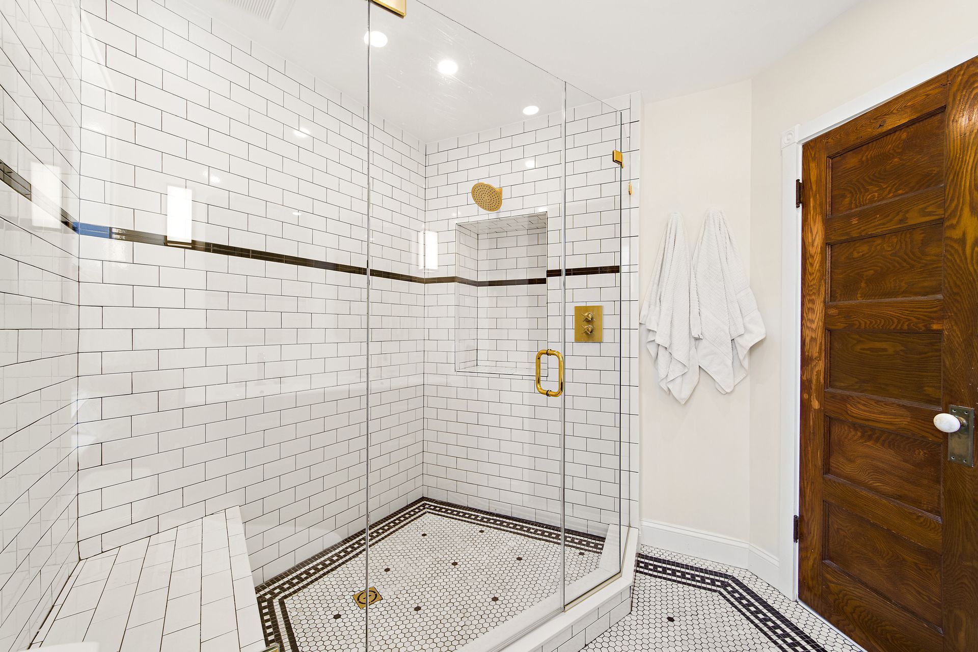 historic bathroom remodel with white subway tile shower, black mosaic floor, gold fixtures, and vintage wood door