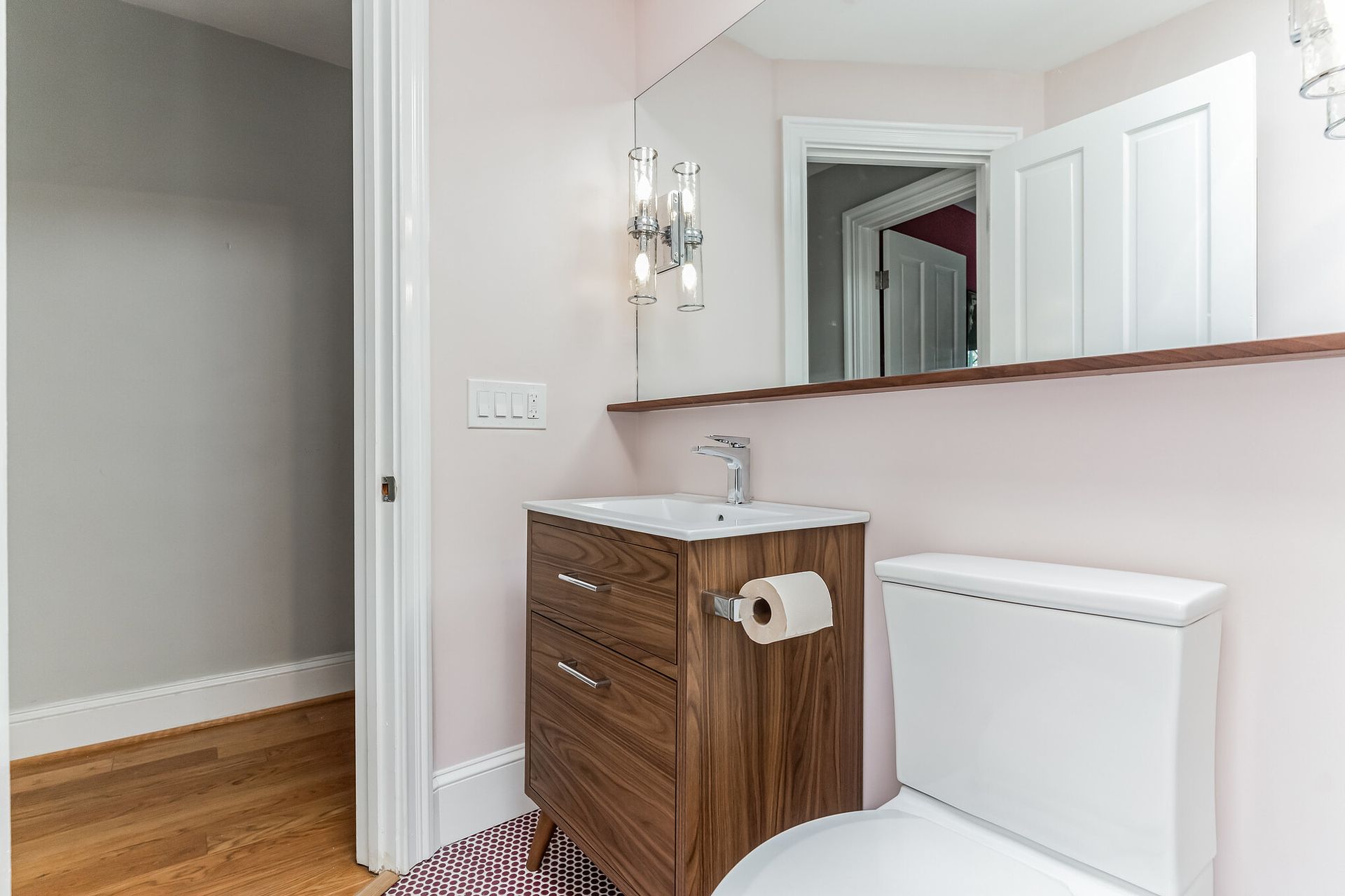 mid-century modern vanity with wood cabinet, integrated sink, large mirror, and pink walls