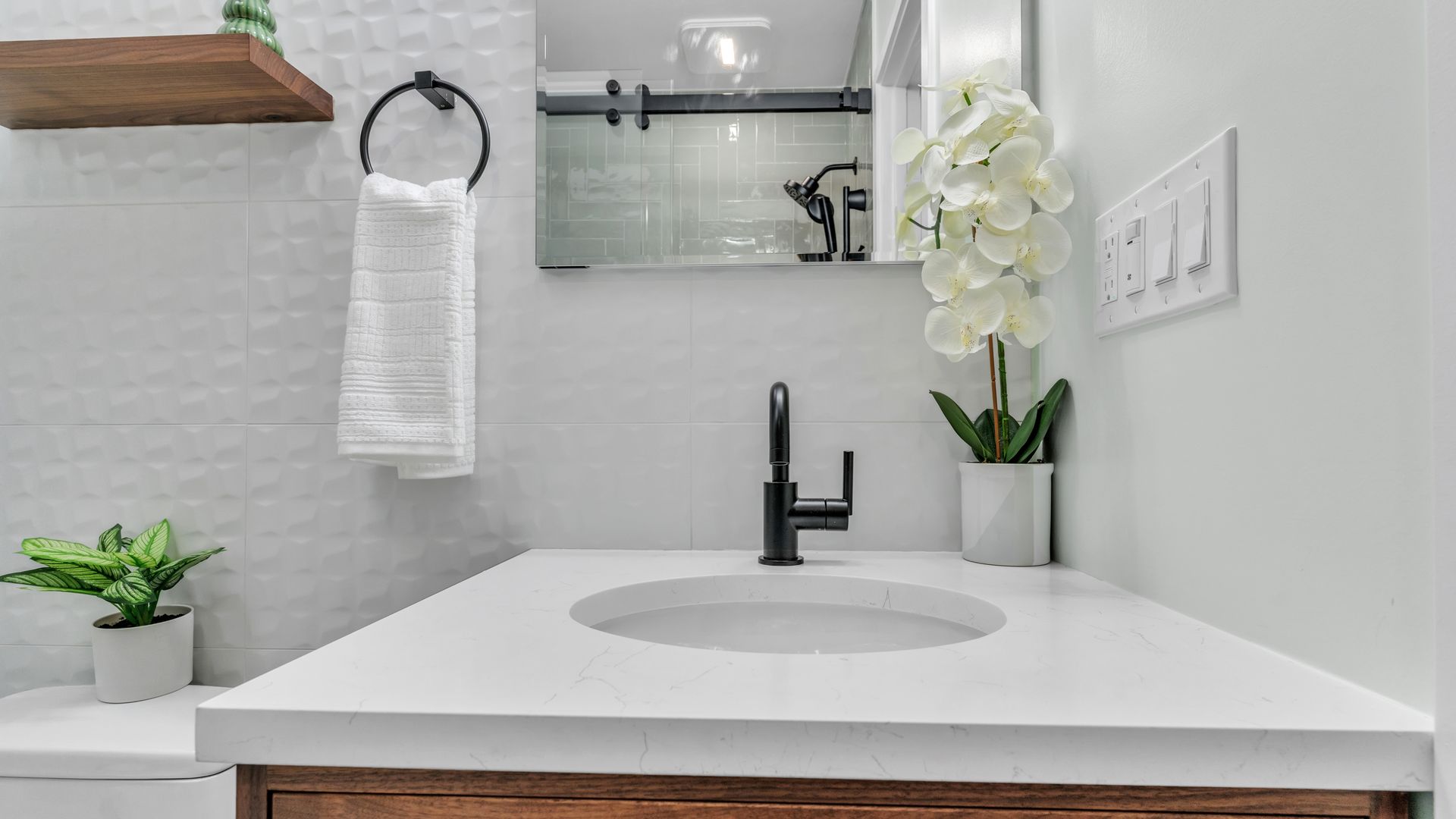 modern DC bathroom vanity with black faucet, floating shelf, textured white tile, orchid decor, remodel inspiration