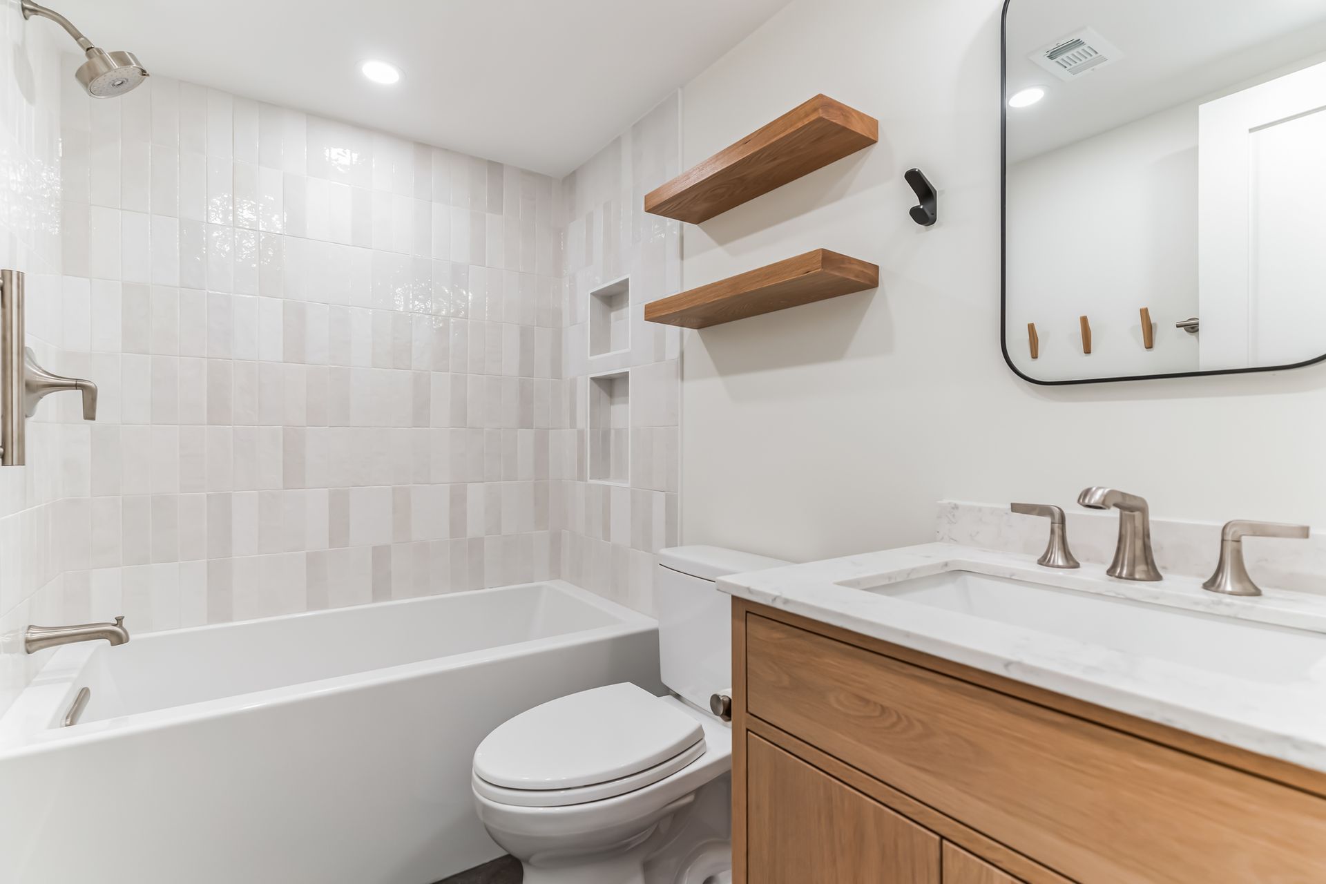 modern bathroom remodel with light tile, wood vanity, floating shelves, built-in shower niches, and brushed nickel fixtures