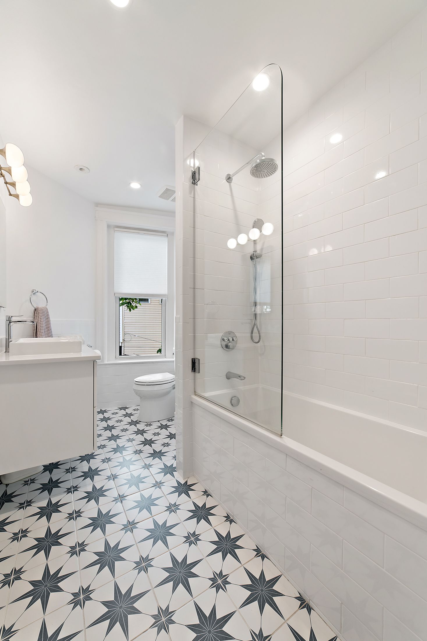modern white bathroom with tub shower combo, glass panel, star-pattern tile floor, and vessel sink in historic DC home remodel