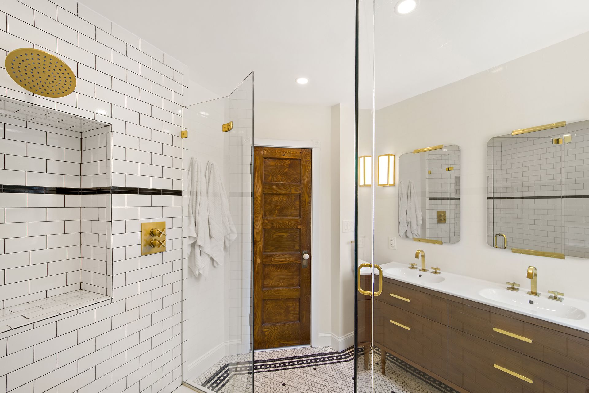 modern bathroom renovation with subway tile shower, brass fixtures, double vanity, and original wood door