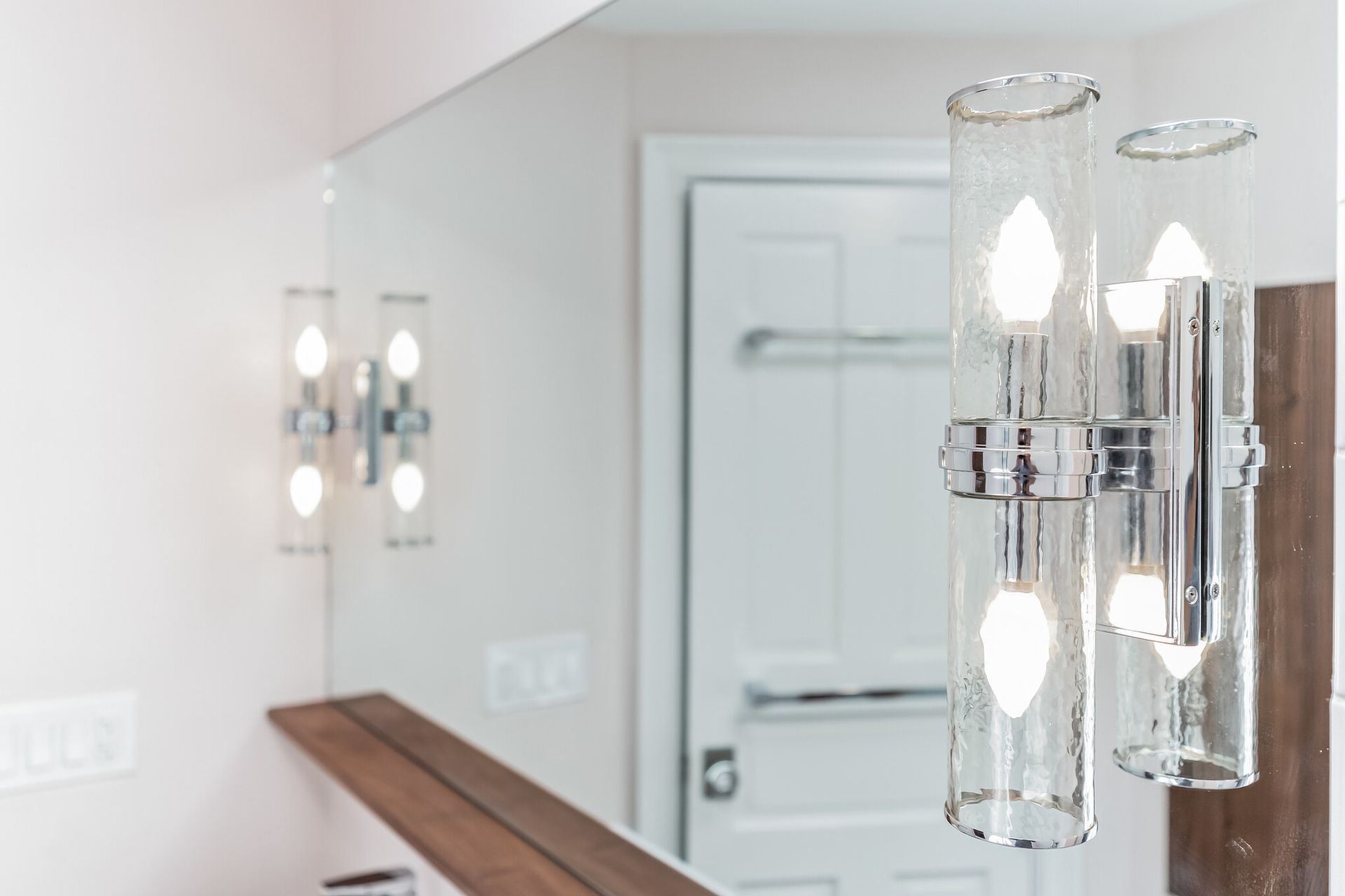 close-up of modern chrome bathroom vanity light with textured glass sconces and reflection in wall mirror