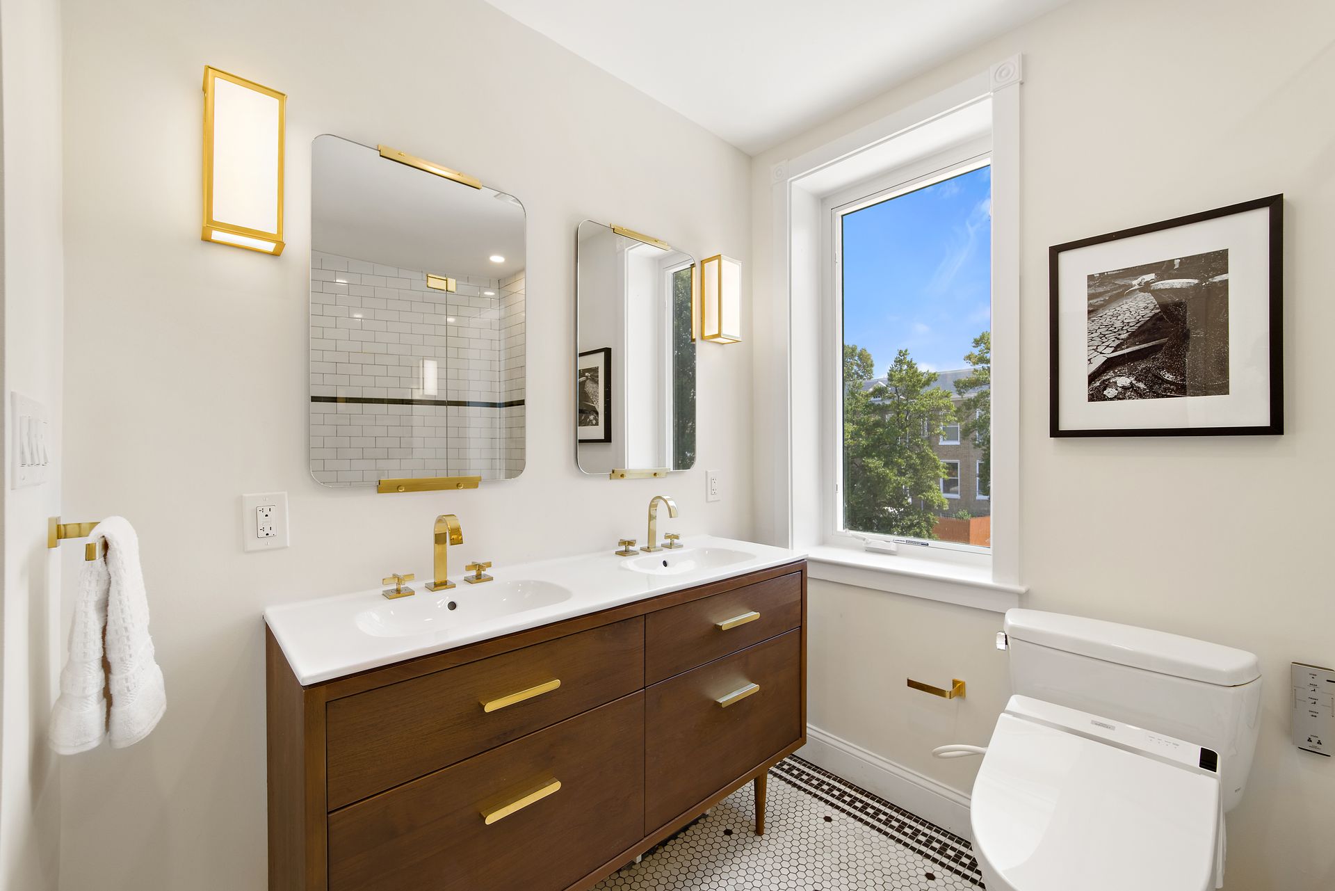 mid-century modern bathroom with gold fixtures, wood vanity, double sinks, and natural light through large window