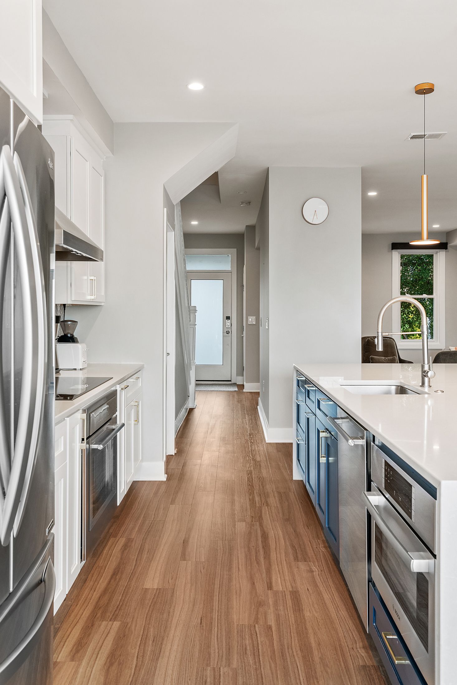 Modern galley kitchen with wood flooring, blue island cabinets, quartz countertops, and white upper cabinetry