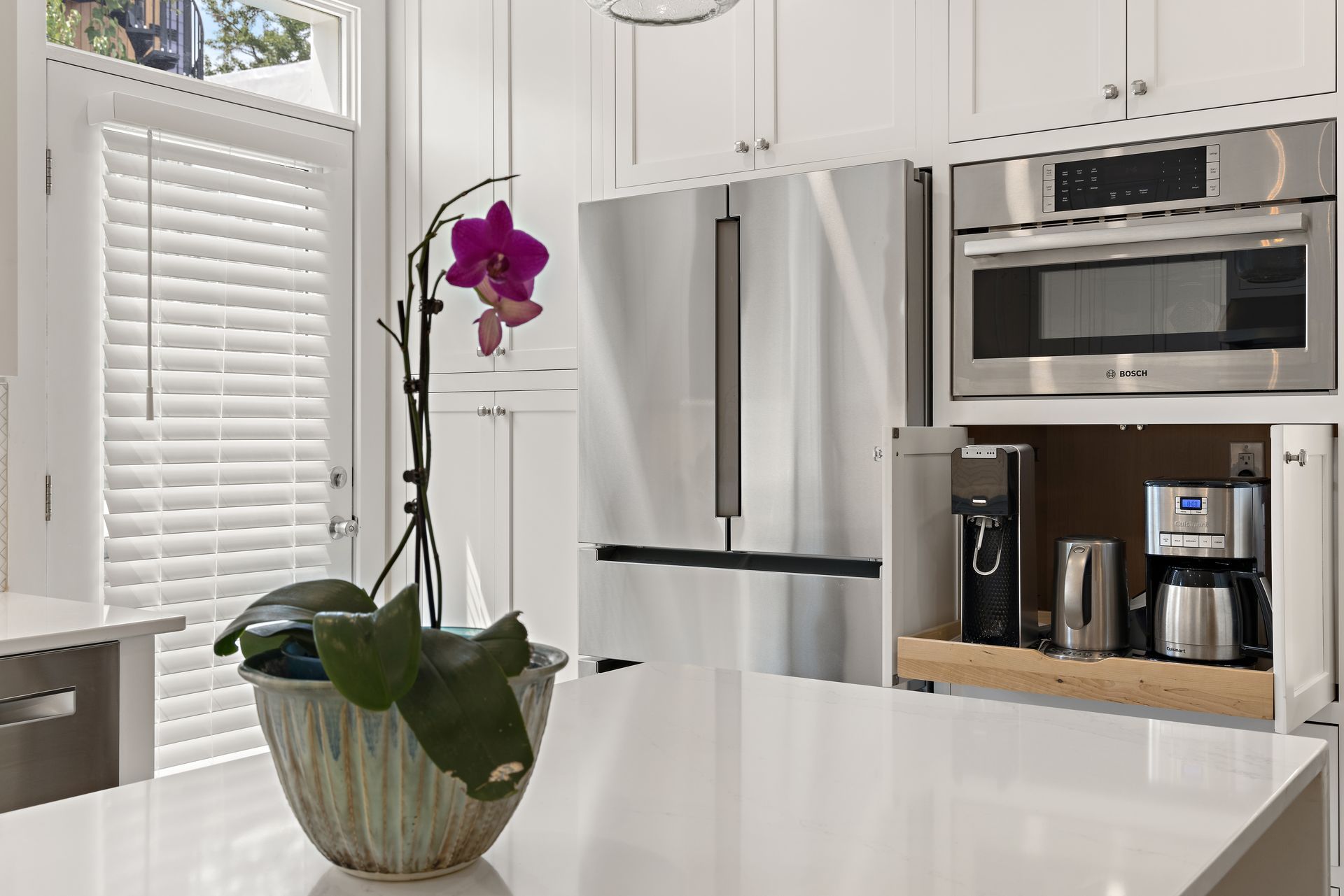 Modern white kitchen with appliance garage and orchid on quartz island