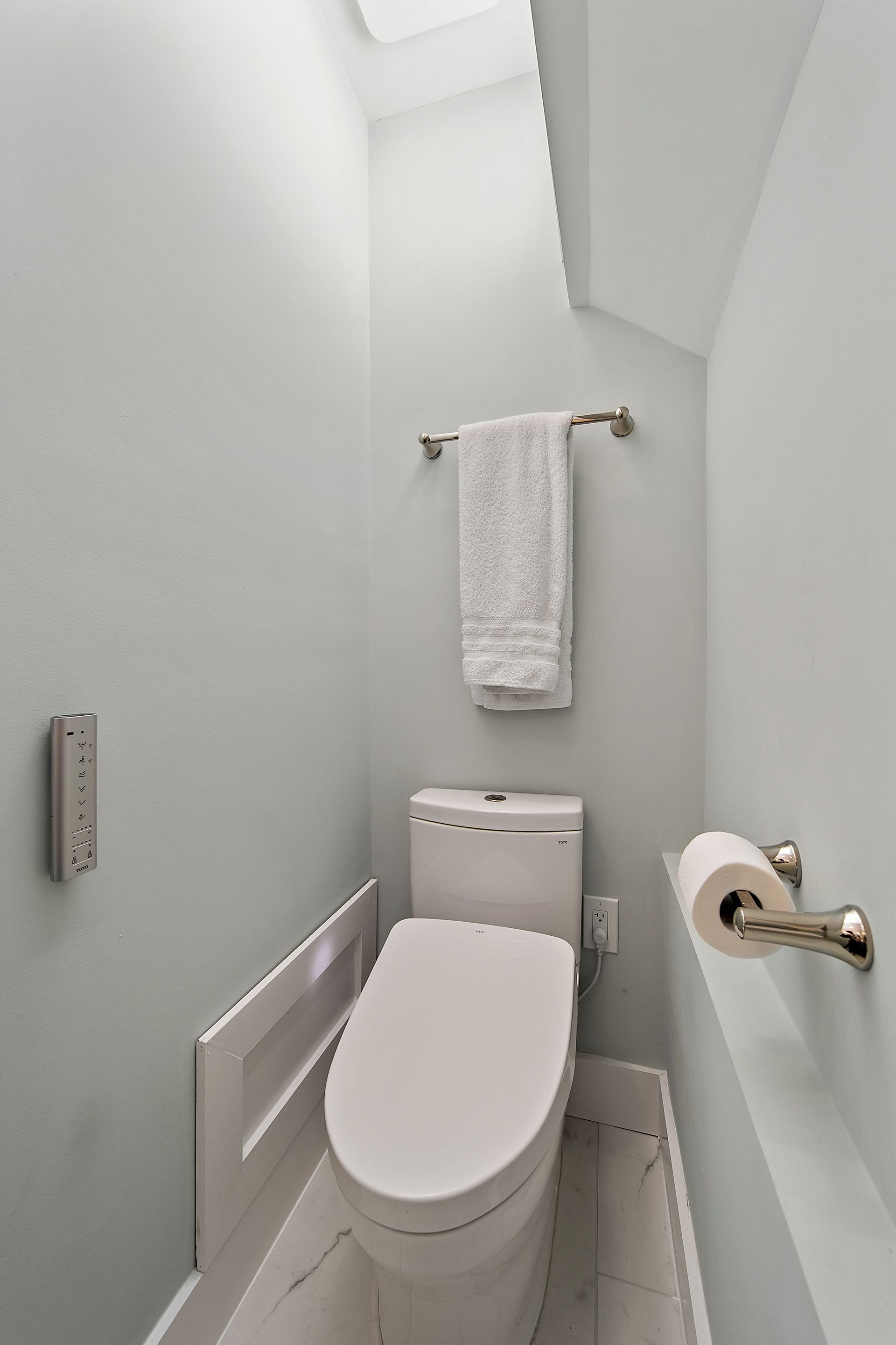 Modern toilet nook with wall-mounted bidet controls, towel bar, and soft blue-gray walls