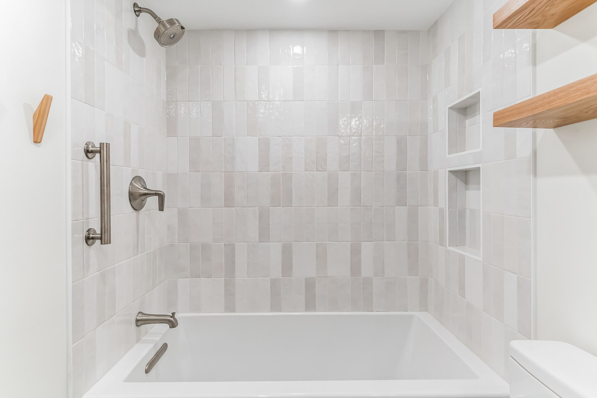 modern tub shower combo with white vertical tile, built-in shower niche, brushed nickel fixtures, and floating wood shelves