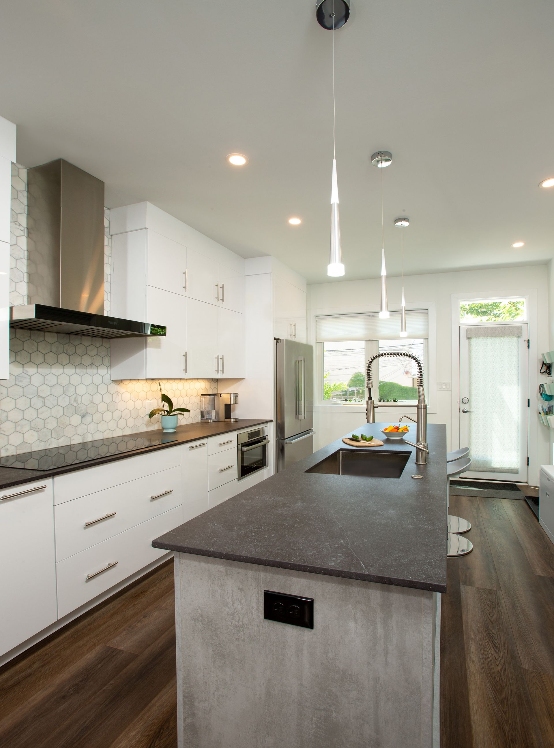 Modern white kitchen with black countertops, hex tile backsplash, and pendant lighting over island