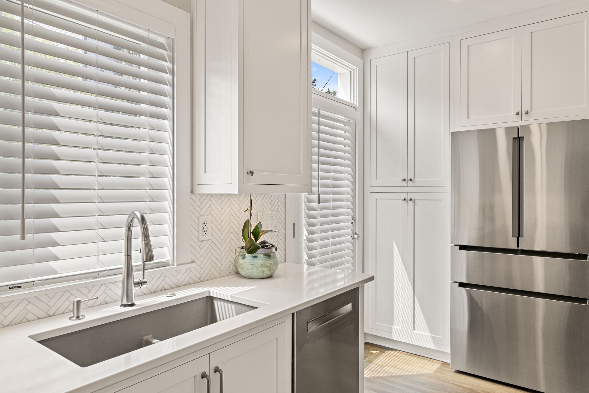 White kitchen with natural light, stainless steel fridge, and herringbone backsplash