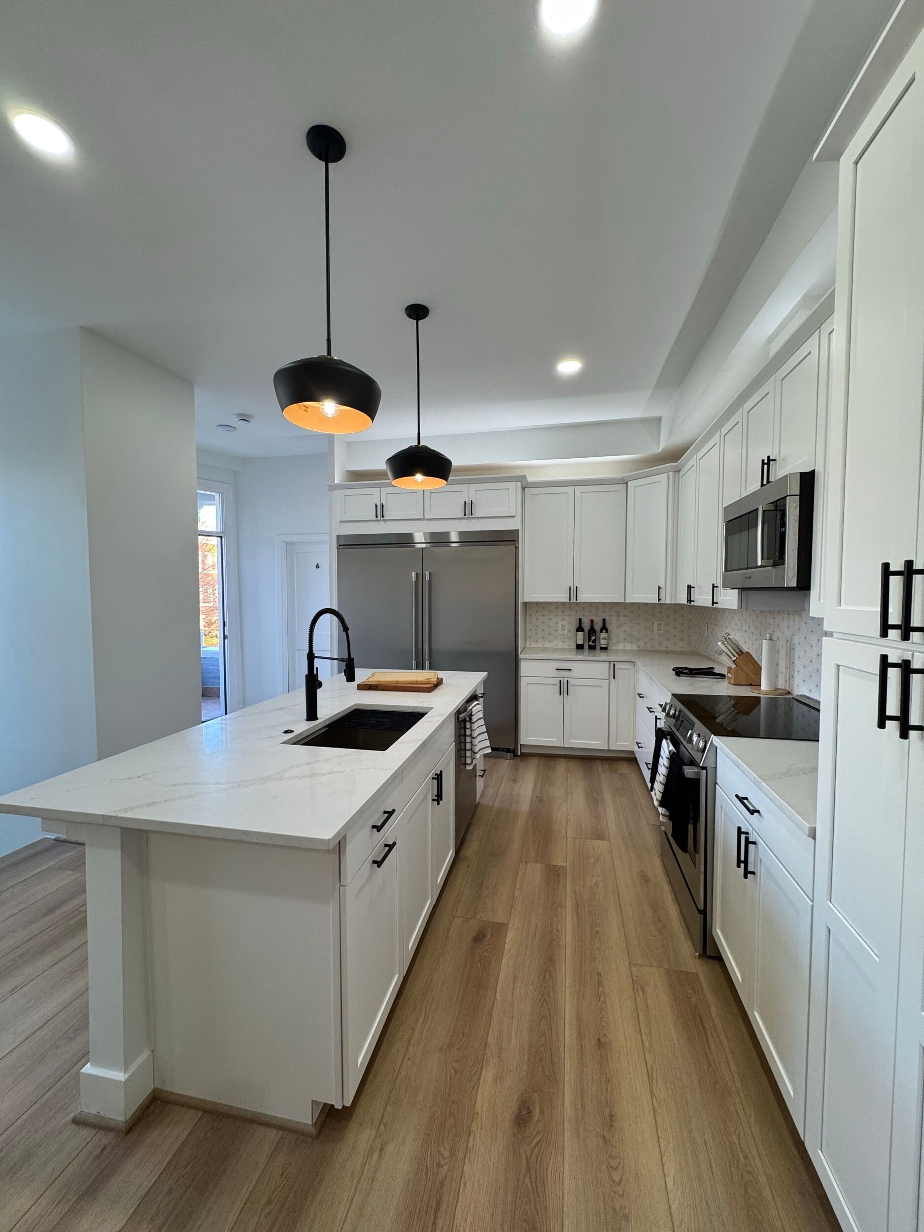 modern white kitchen with island, black fixtures, pendant lighting, quartz countertops, wood floors, custom cabinets
