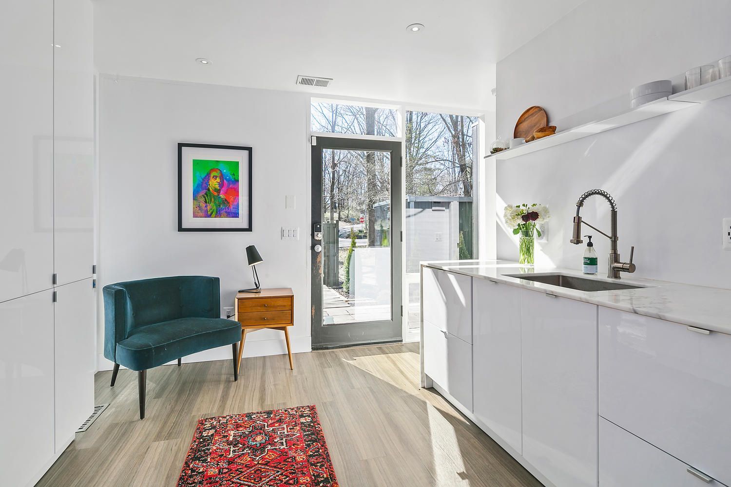 modern white kitchen with glossy cabinets, quartz counters, tall window door, and velvet accent chair