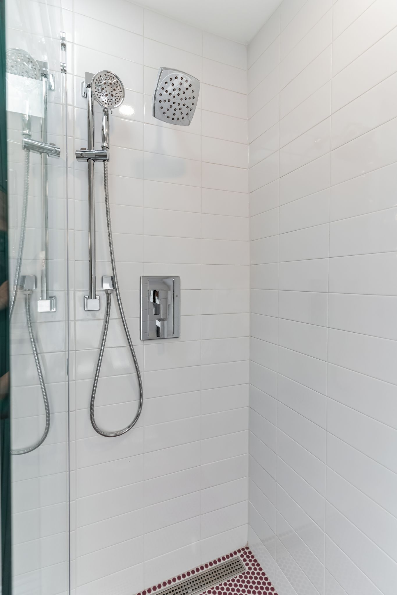 white tile shower with handheld and wall-mounted chrome showerheads and red penny tile floor