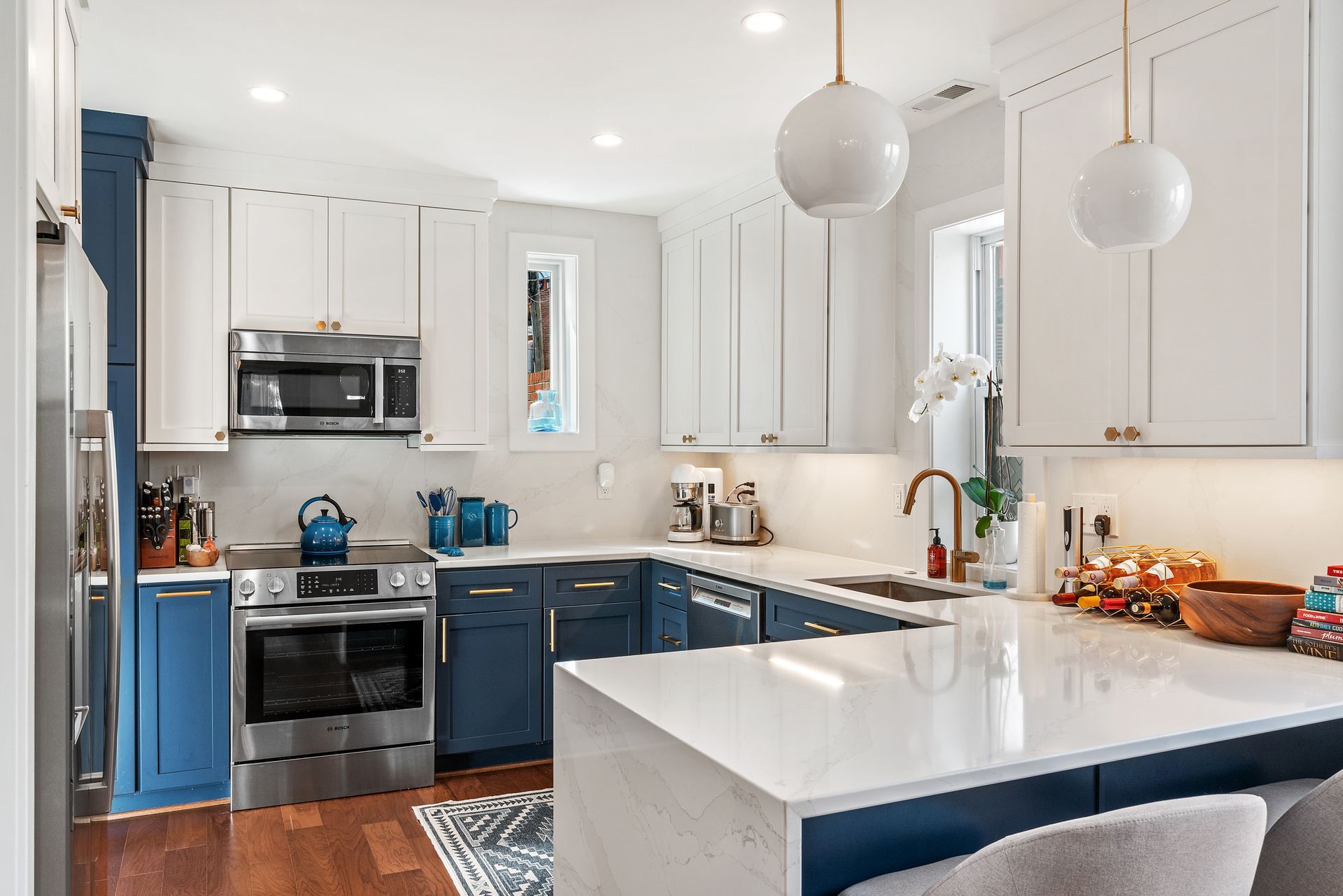 Navy and white kitchen with shaker cabinets, quartz waterfall peninsula, gold hardware, and modern pendant lights