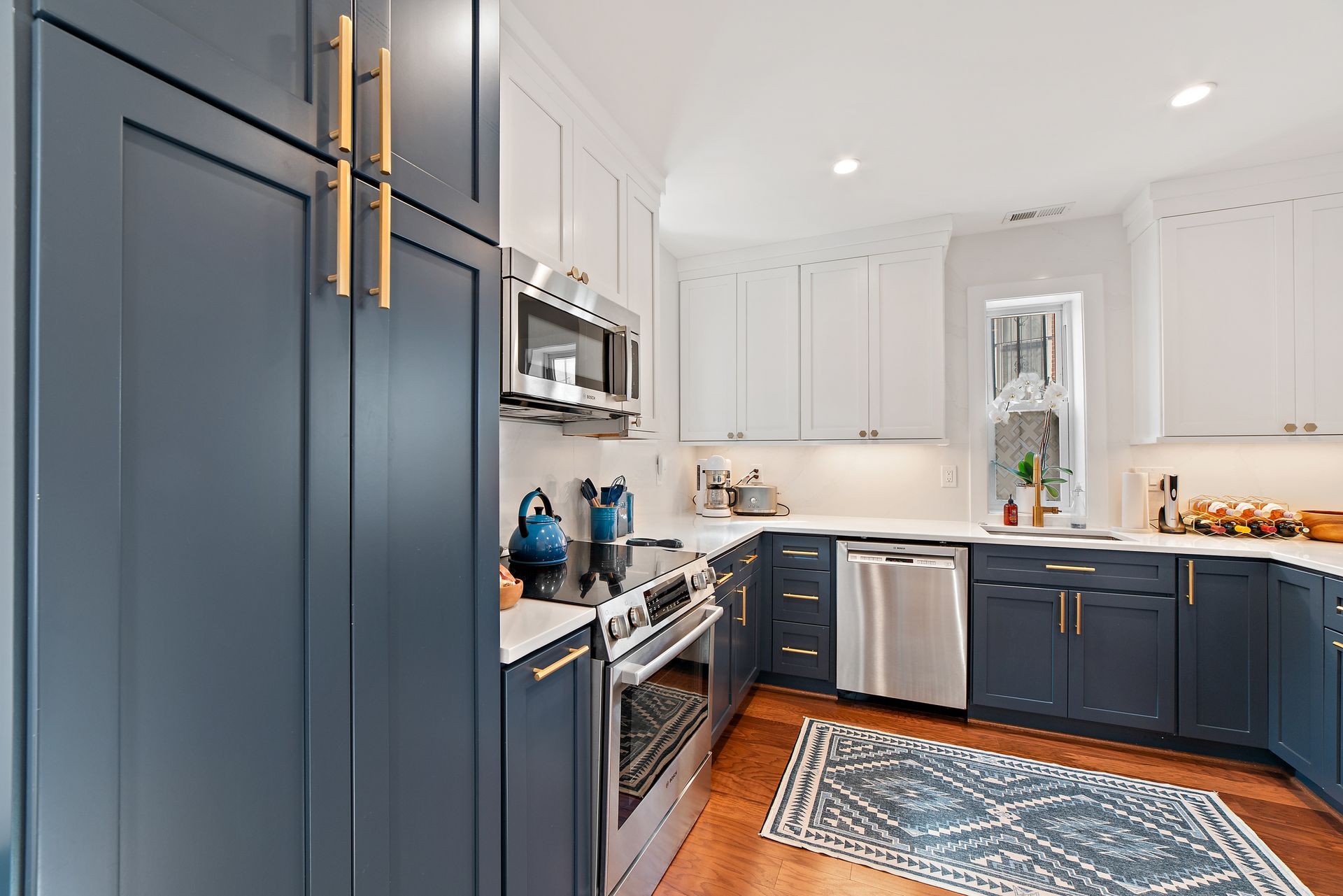 navy kitchen cabinets with gold hardware, white countertops, U-shaped layout, and stainless steel appliances