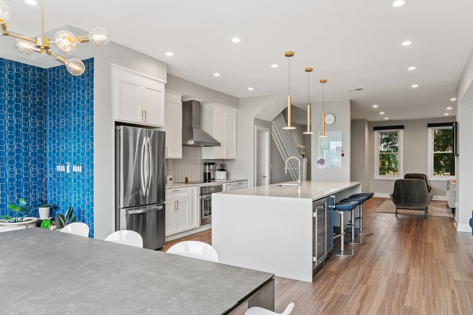 Open concept kitchen with white cabinets, waterfall island, blue accent tile wall, and gold pendant lights in DC row house
