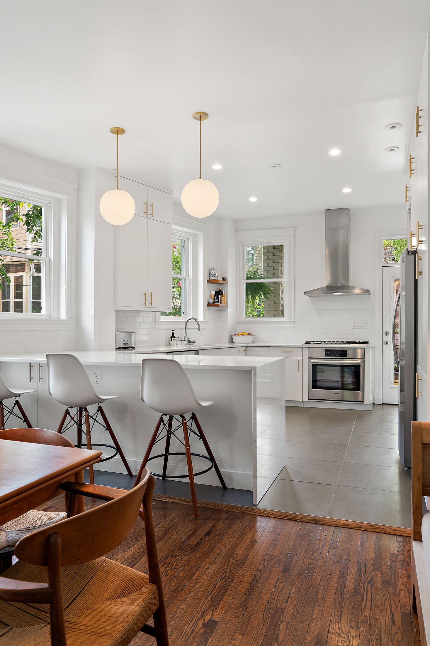 Open-concept kitchen with waterfall island, white cabinetry, globe pendant lights, and Eames-style bar stools overlooking dining area and stainless steel appliances.