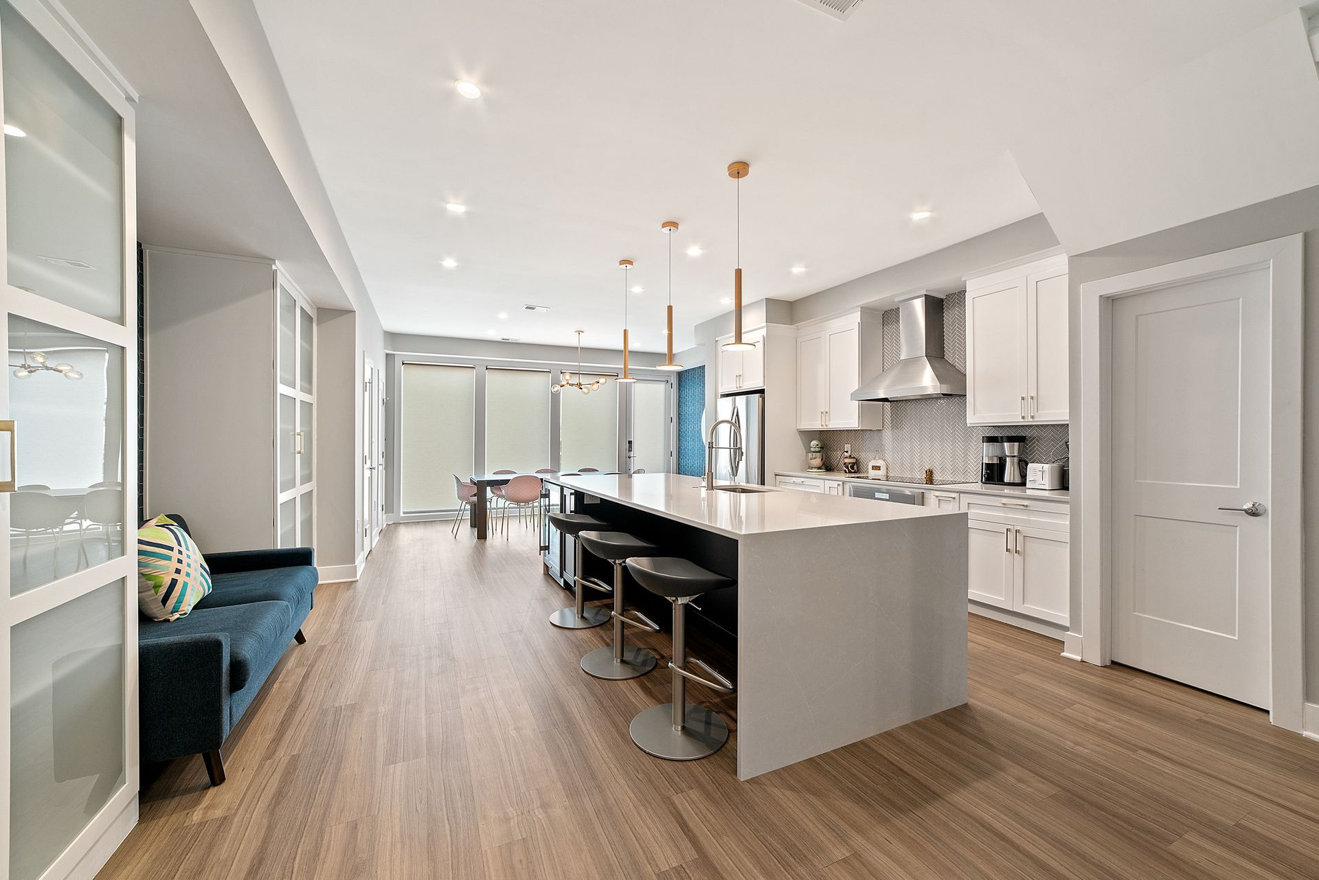 Open kitchen layout with waterfall island, modern pendant lights, white cabinets, and warm wood flooring