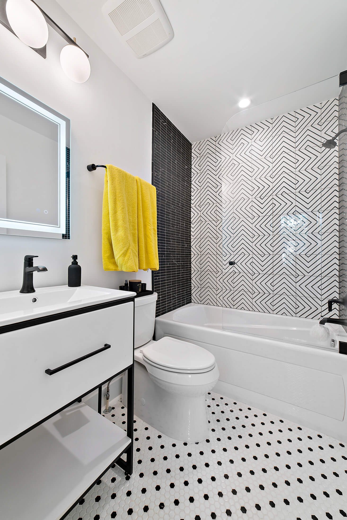 hall bathroom with modern black and white tile, geometric shower surround, and yellow towel accent