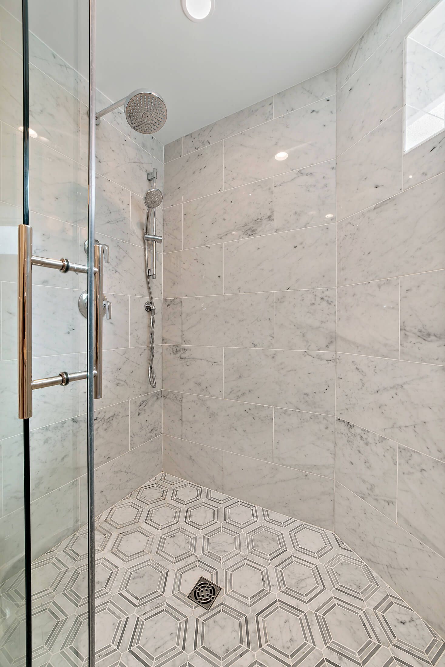 marble tile walk-in shower with dual showerheads and glass door in updated guest bathroom remodel