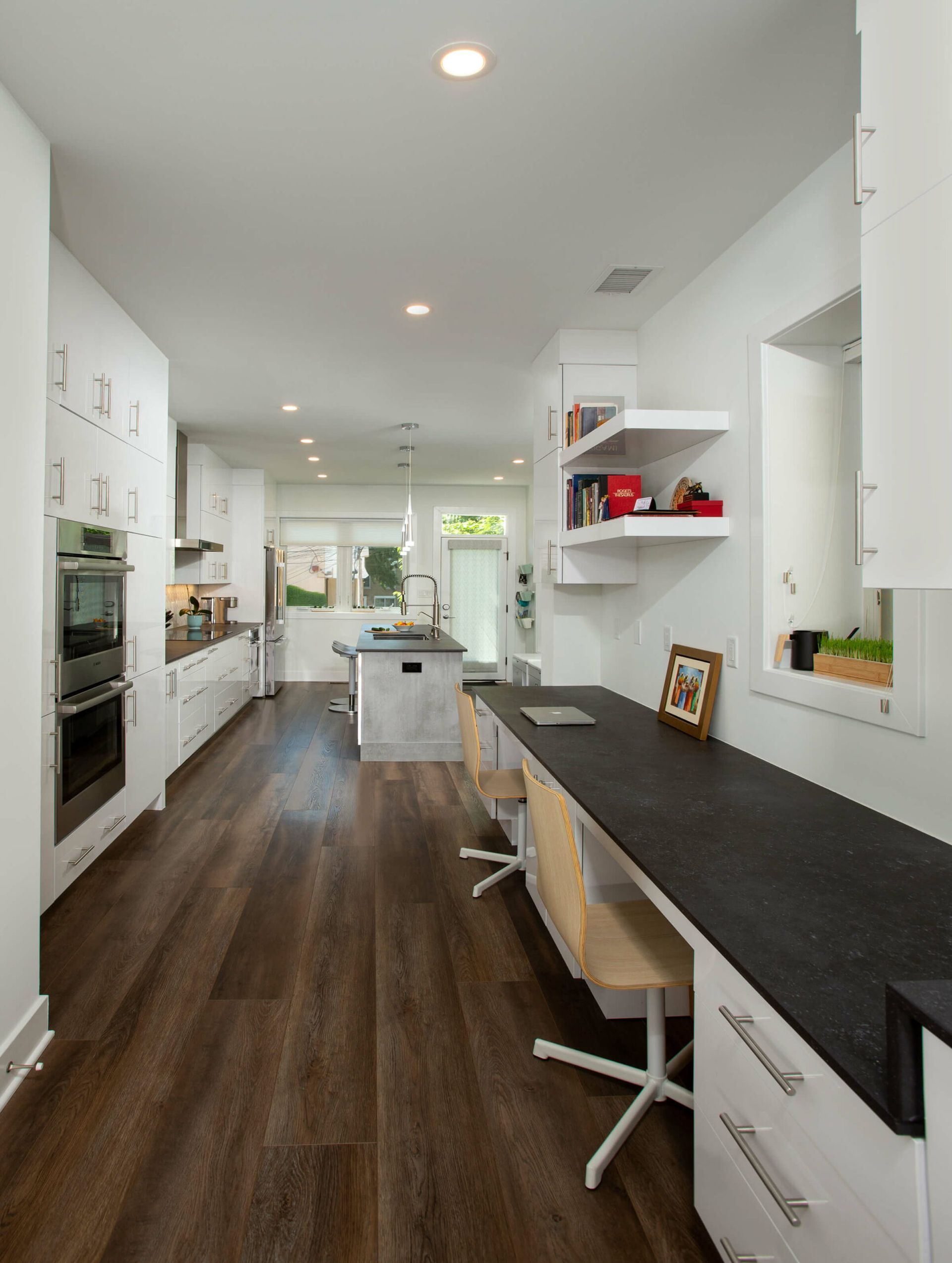 Modern kitchen with built-in desk workspace, dark countertops, and double oven