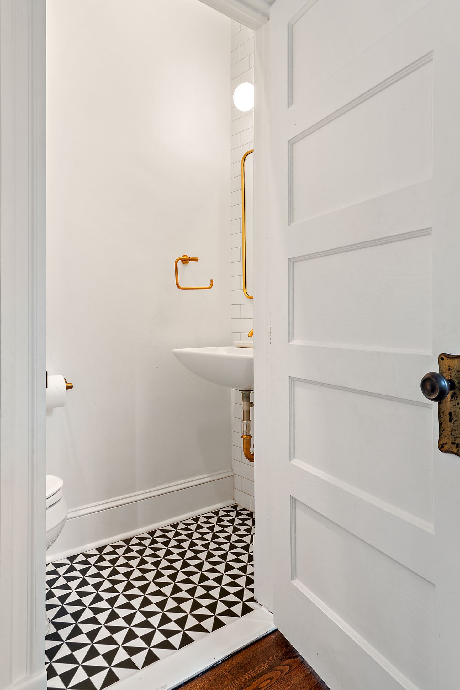 small powder room remodel with black and white geometric tile, wall-mounted sink, and orange gold bathroom fixtures