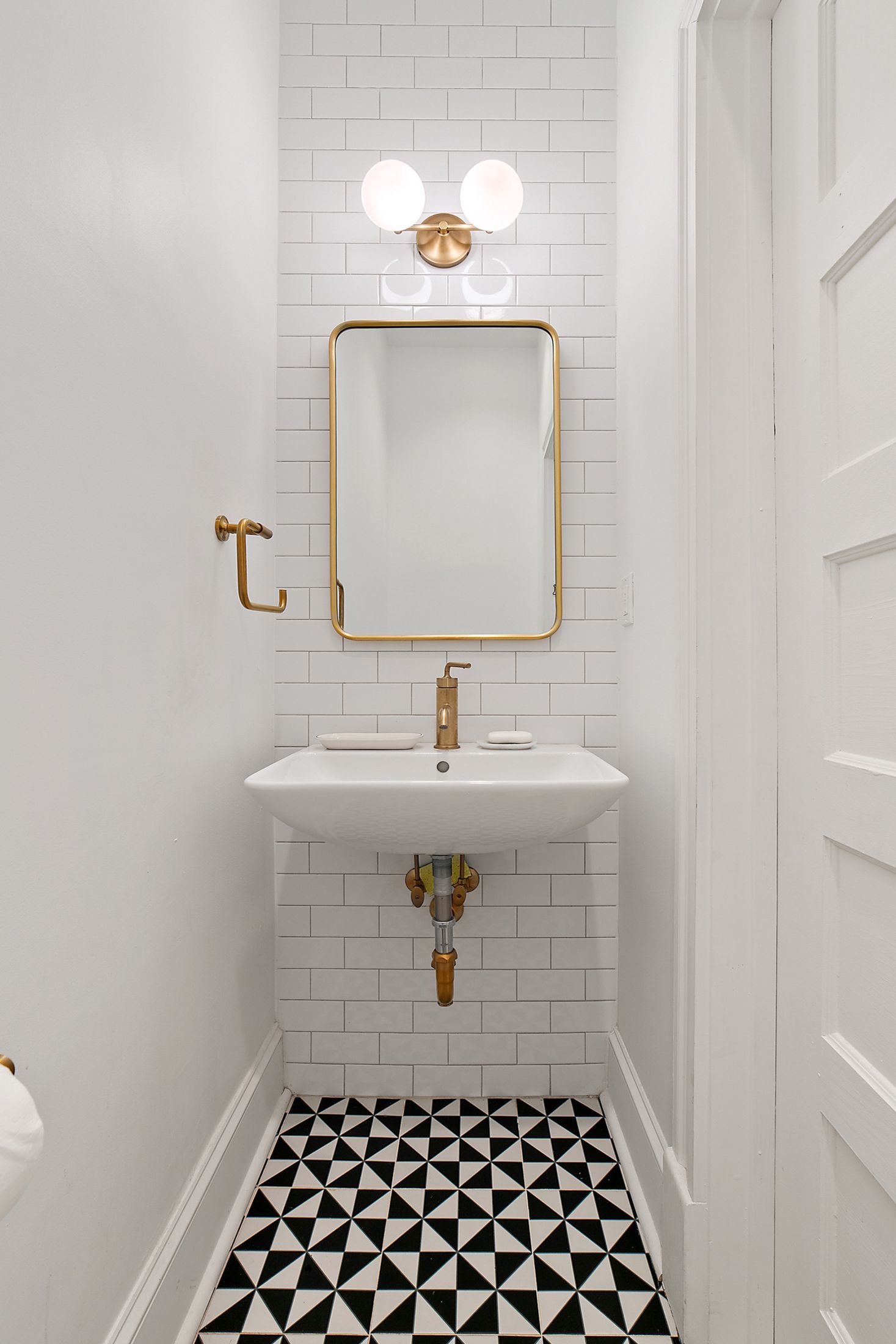 modern powder room remodel with wall-mounted sink, gold faucet and mirror, subway tile wall, and geometric black and white tile floor