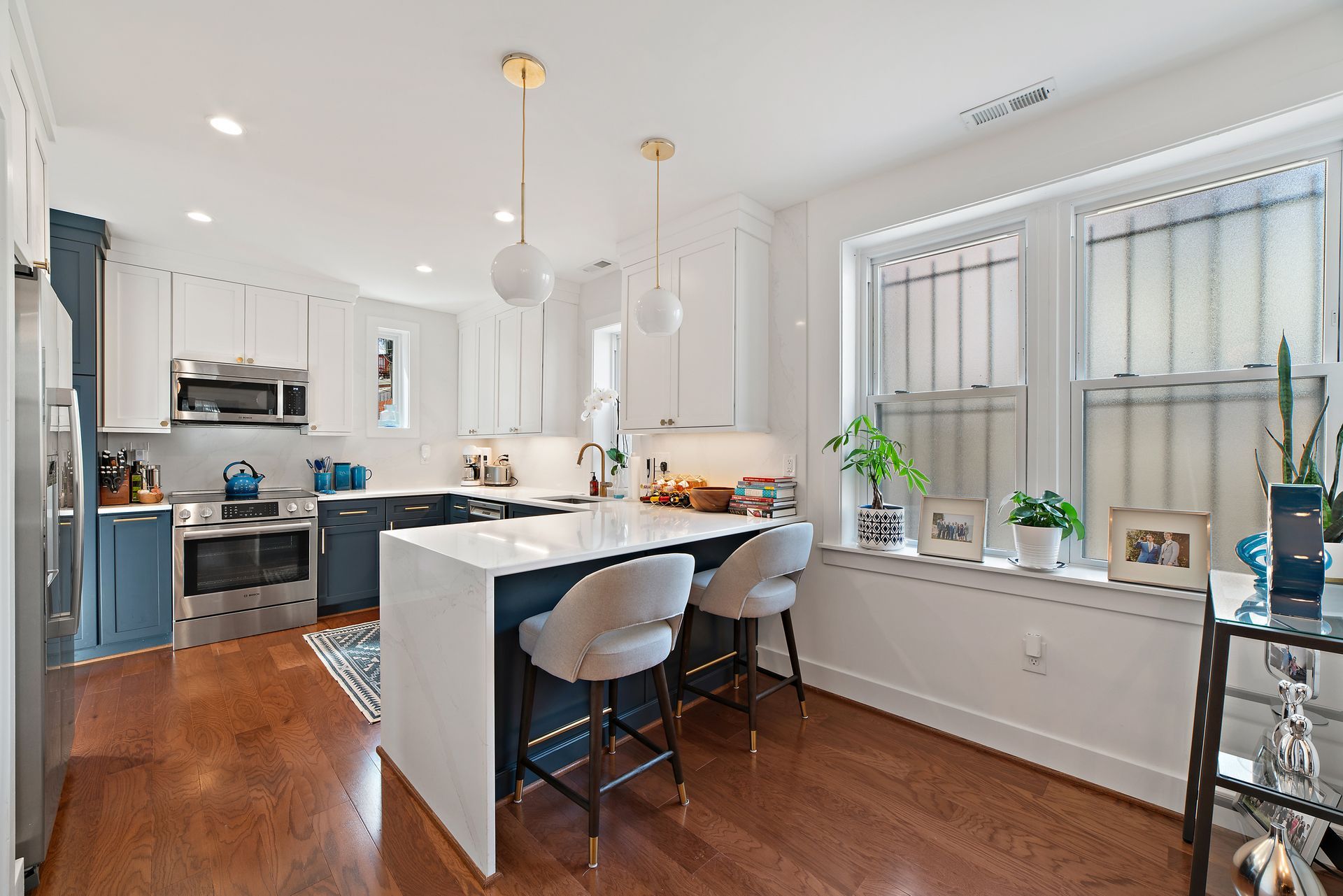 Two-tone kitchen with navy blue lower cabinets, white upper cabinets, and a waterfall peninsula breakfast bar
