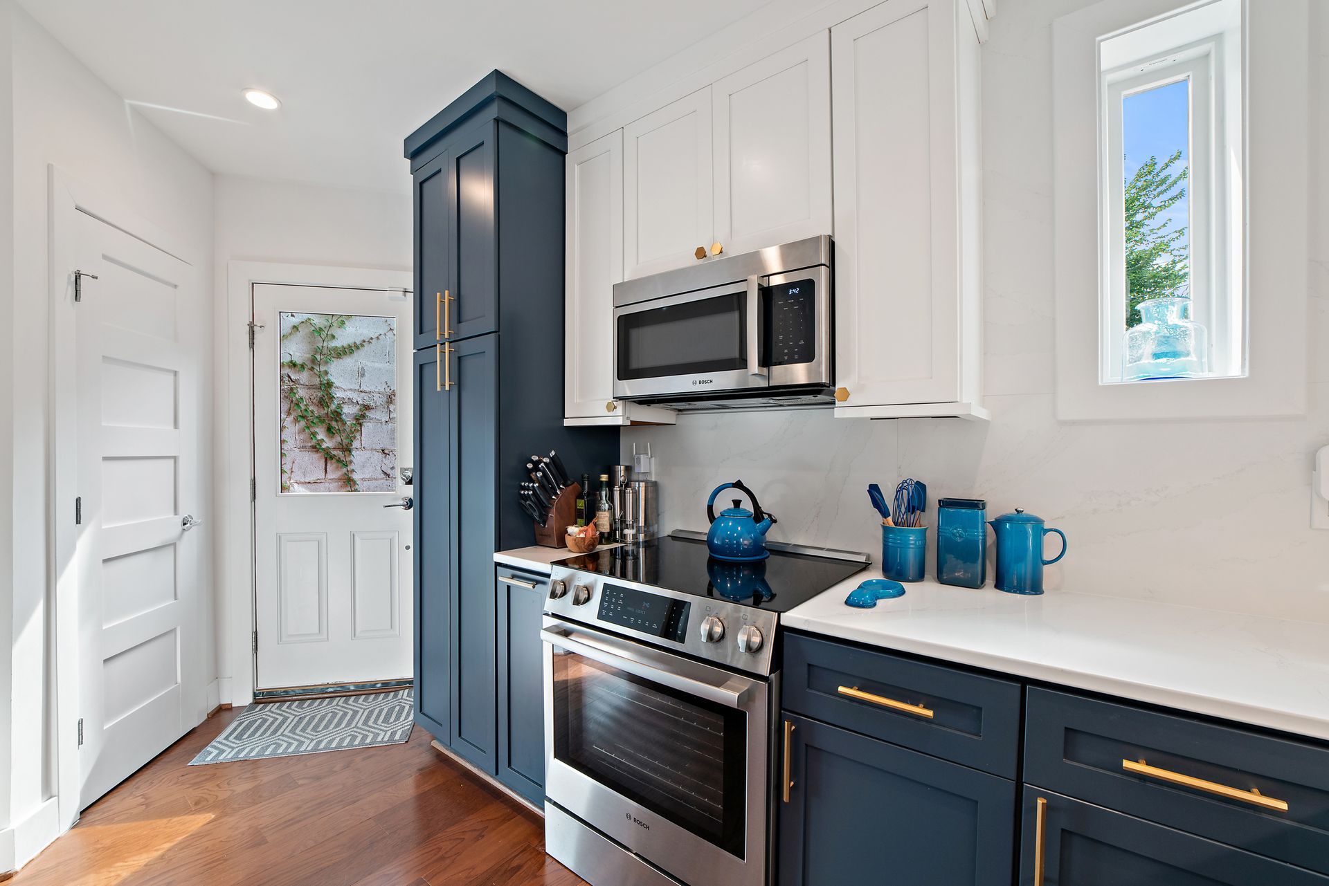 Navy and white kitchen with modern stove, tall pantry cabinet, and gold hardware in a Washington DC row house renovation