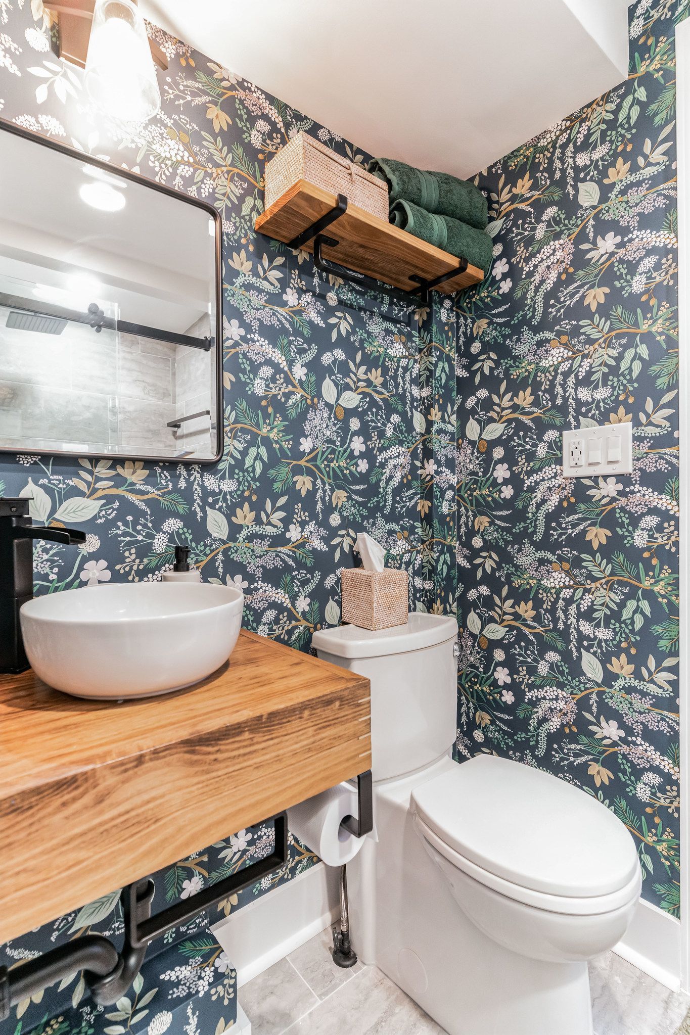 compact bathroom with vessel sink vanity, over-toilet wood shelf, and bold floral wallpaper in green, gold, and white tones