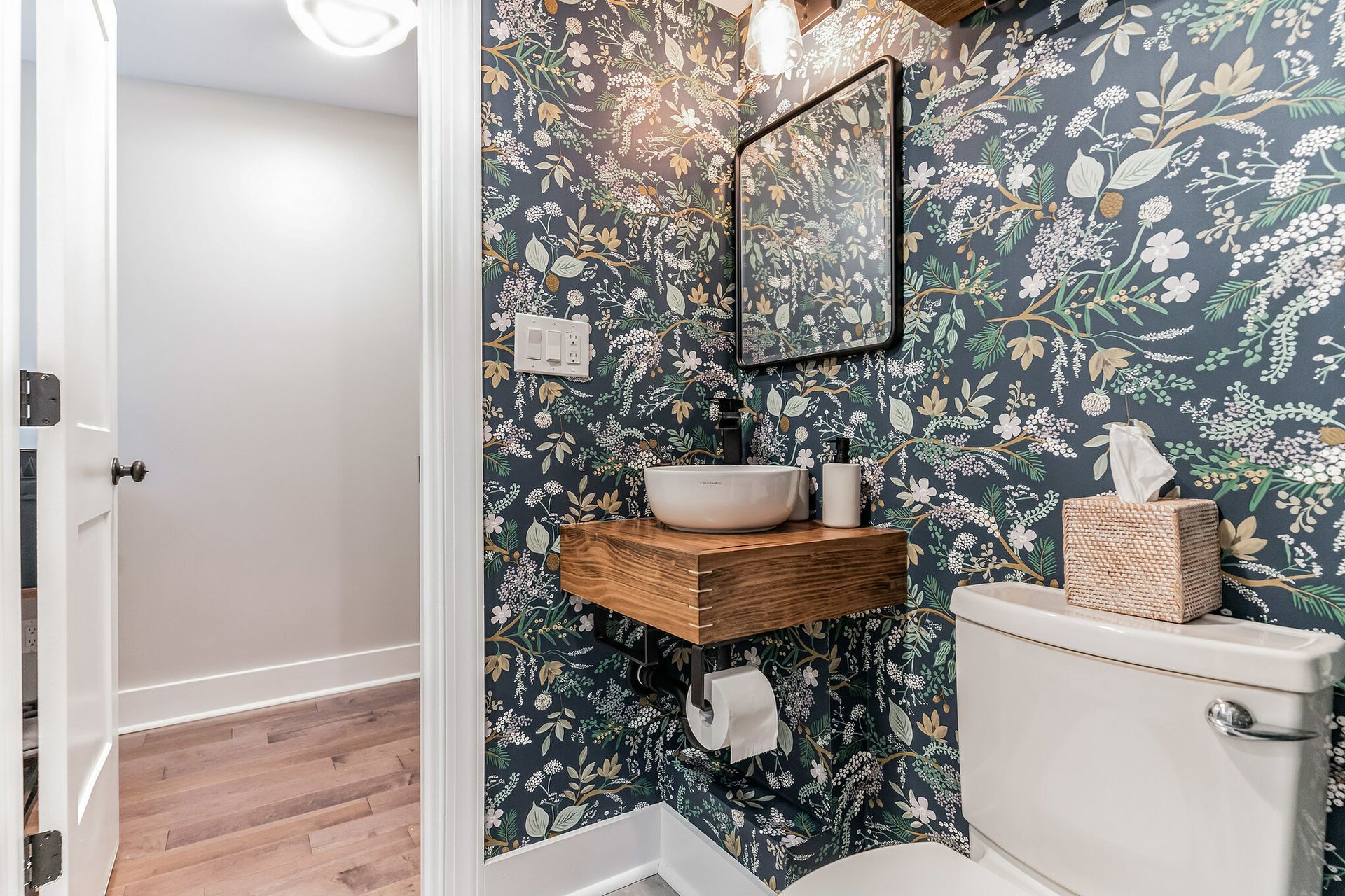 small bathroom with bold floral wallpaper, floating wood vanity, vessel sink, matte black faucet, and rectangular mirror