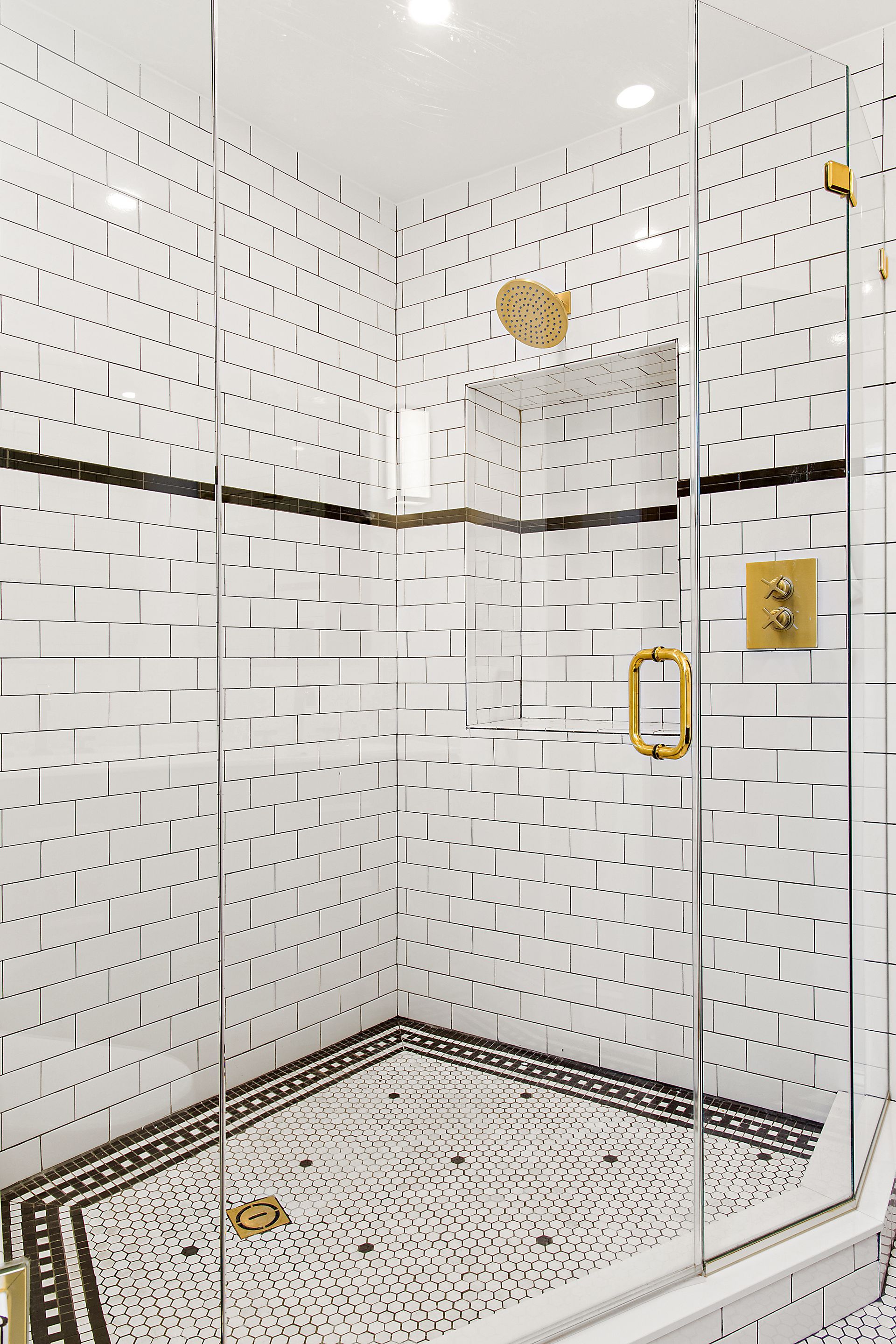 vintage white tile shower with gold fixtures, glass door, black border tile, and built-in shower niche