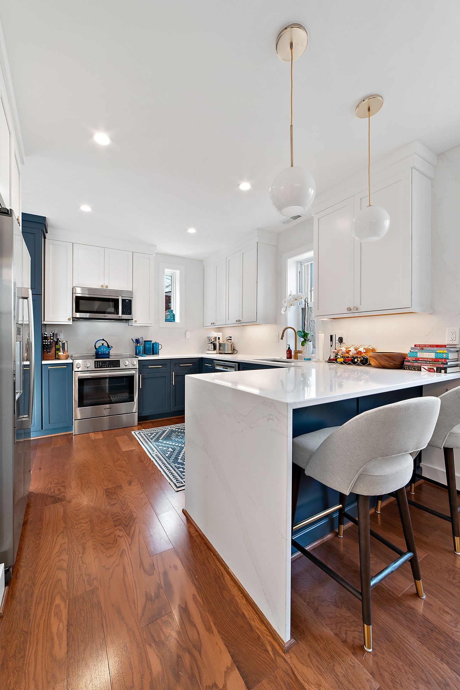 White waterfall peninsula with navy and white cabinets, globe pendants, and warm wood floors in remodeled DC kitchen