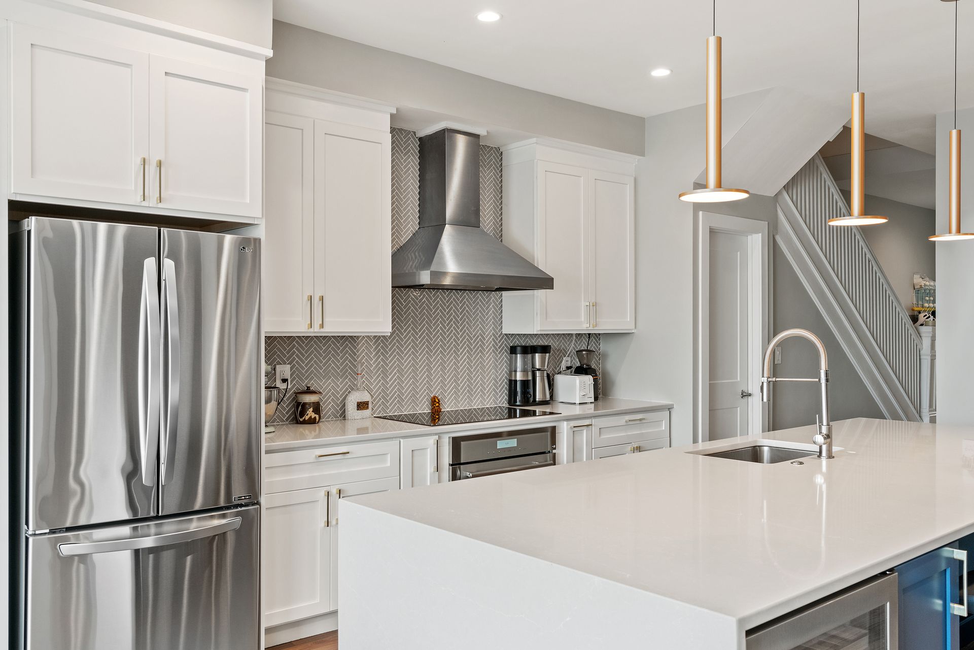 White kitchen with herringbone backsplash, stainless appliances, large island, and modern pendant lighting