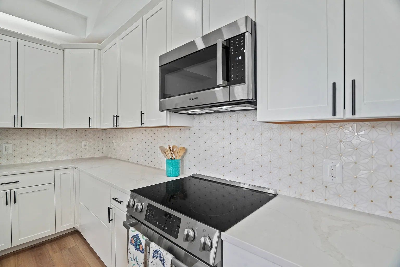 white kitchen with quartz countertops, geometric tile backsplash, black cabinet hardware, Bosch microwave, modern design