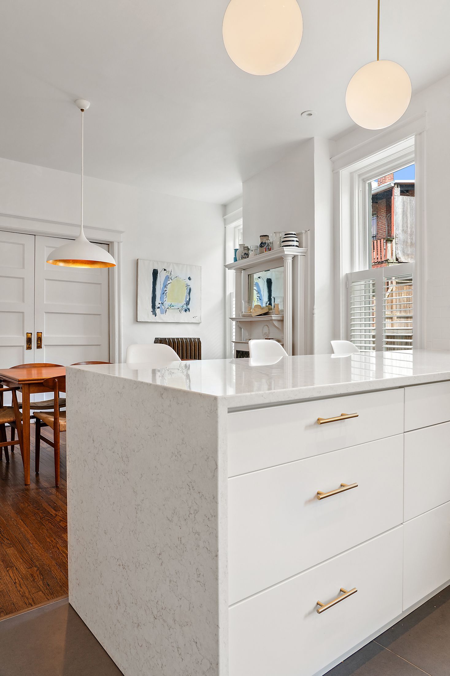 Close-up of a white marble waterfall island in a transitional kitchen with modern pendant lighting and adjacent dining area.