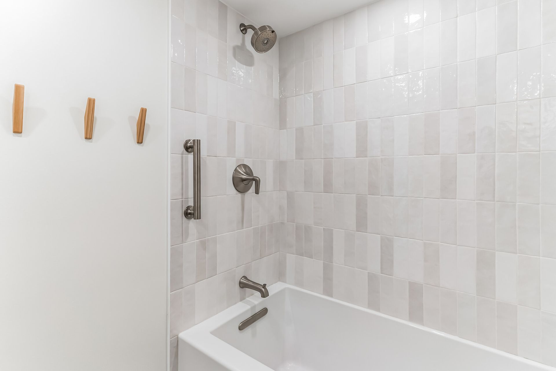 white vertical tile shower wall with brushed nickel fixtures and built-in safety grab bar for bathroom remodel inspiration
