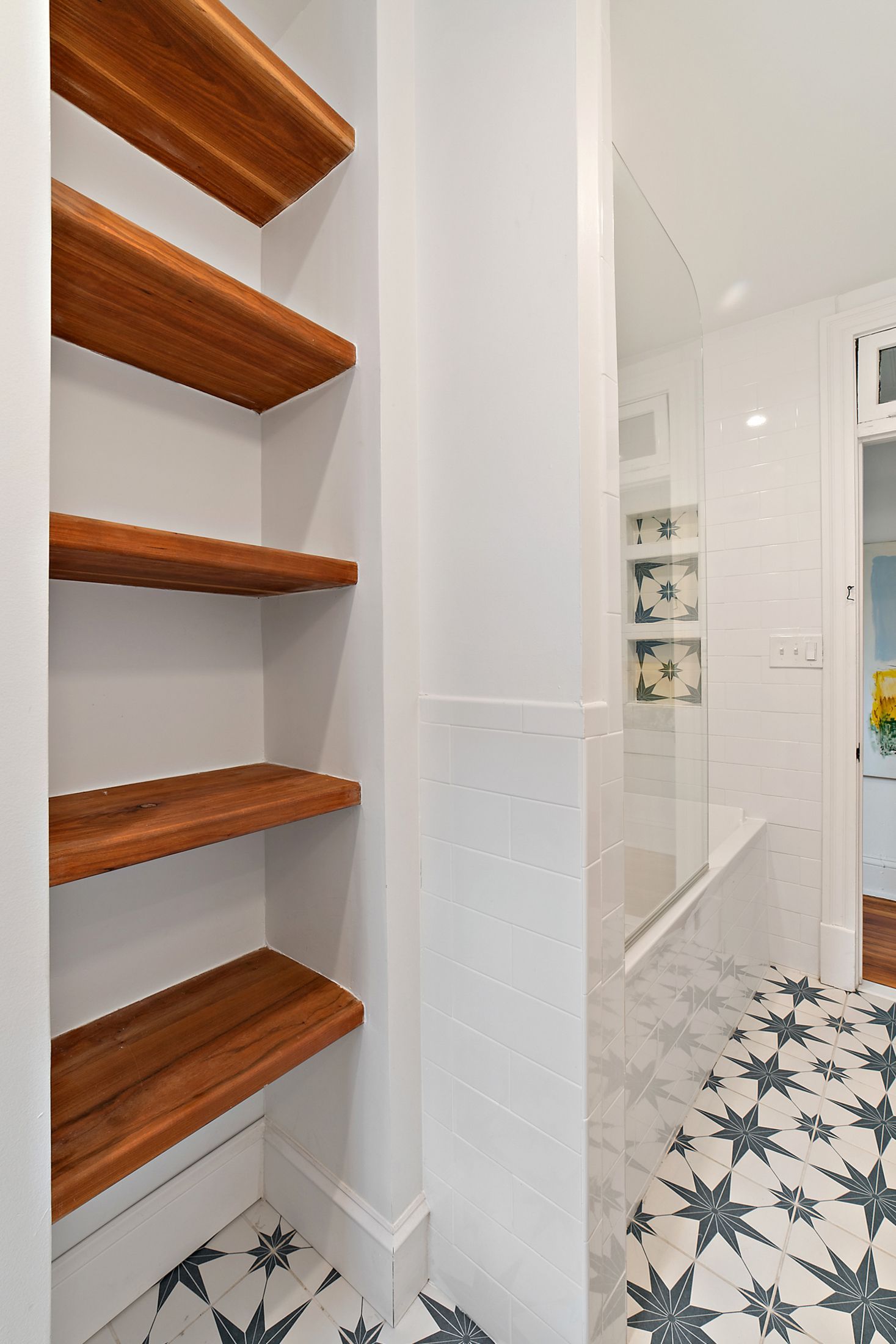 Built-in wood shelves in white bathroom with patterned tile floor and partial view of tub with star tile accent