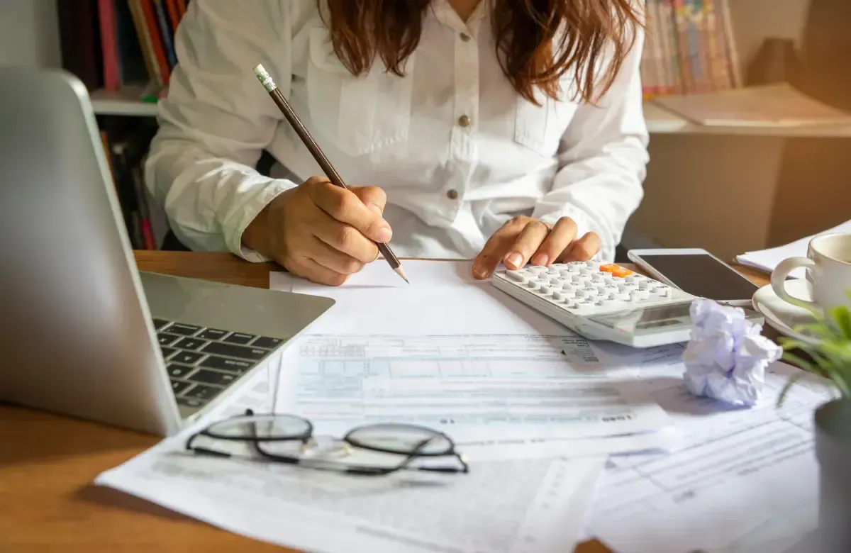 Woman in white shirt working at desk with calculator, pen, and documents.