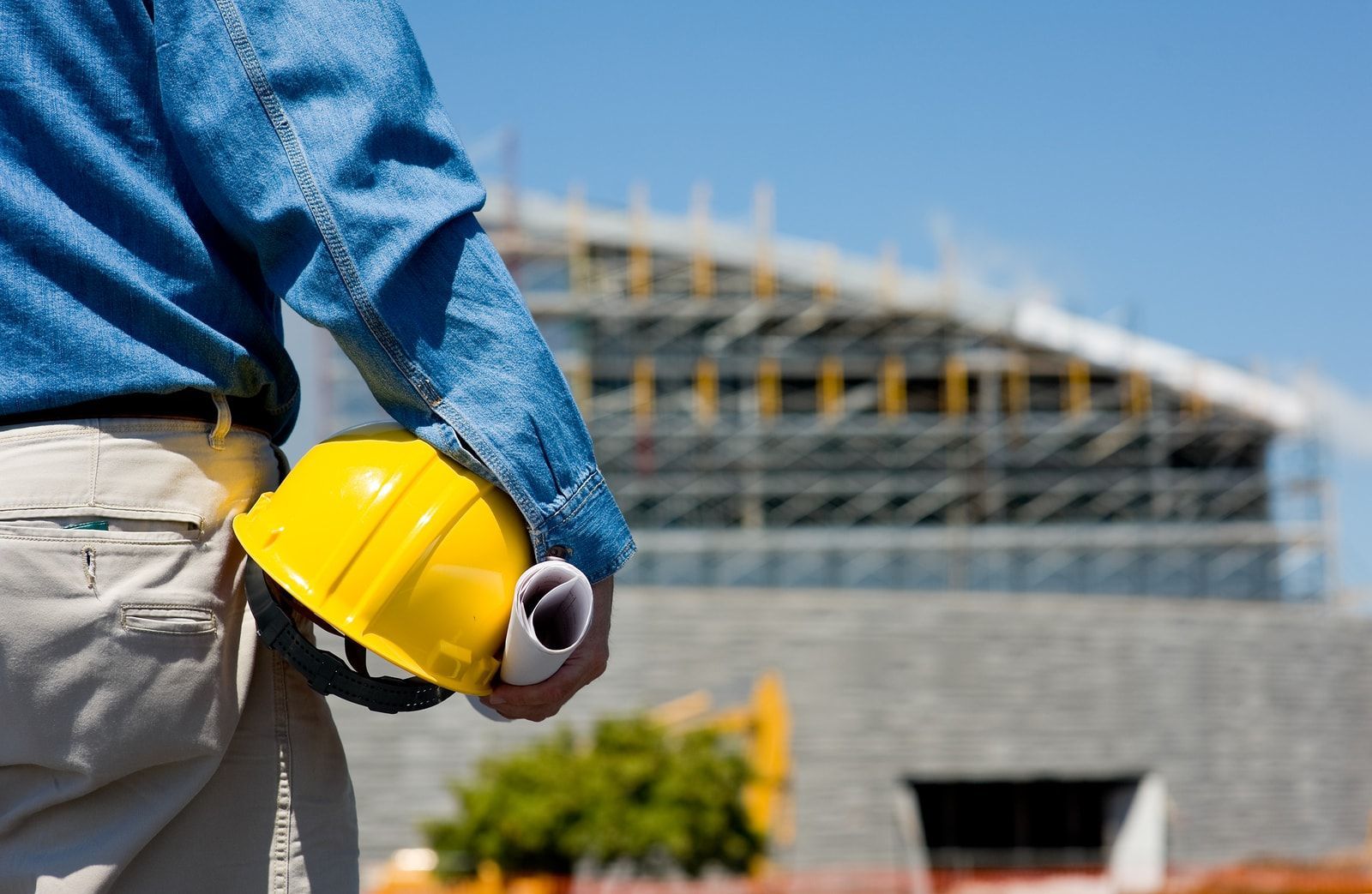 Construction worker with yellow hard hat and blueprints, construction site background.